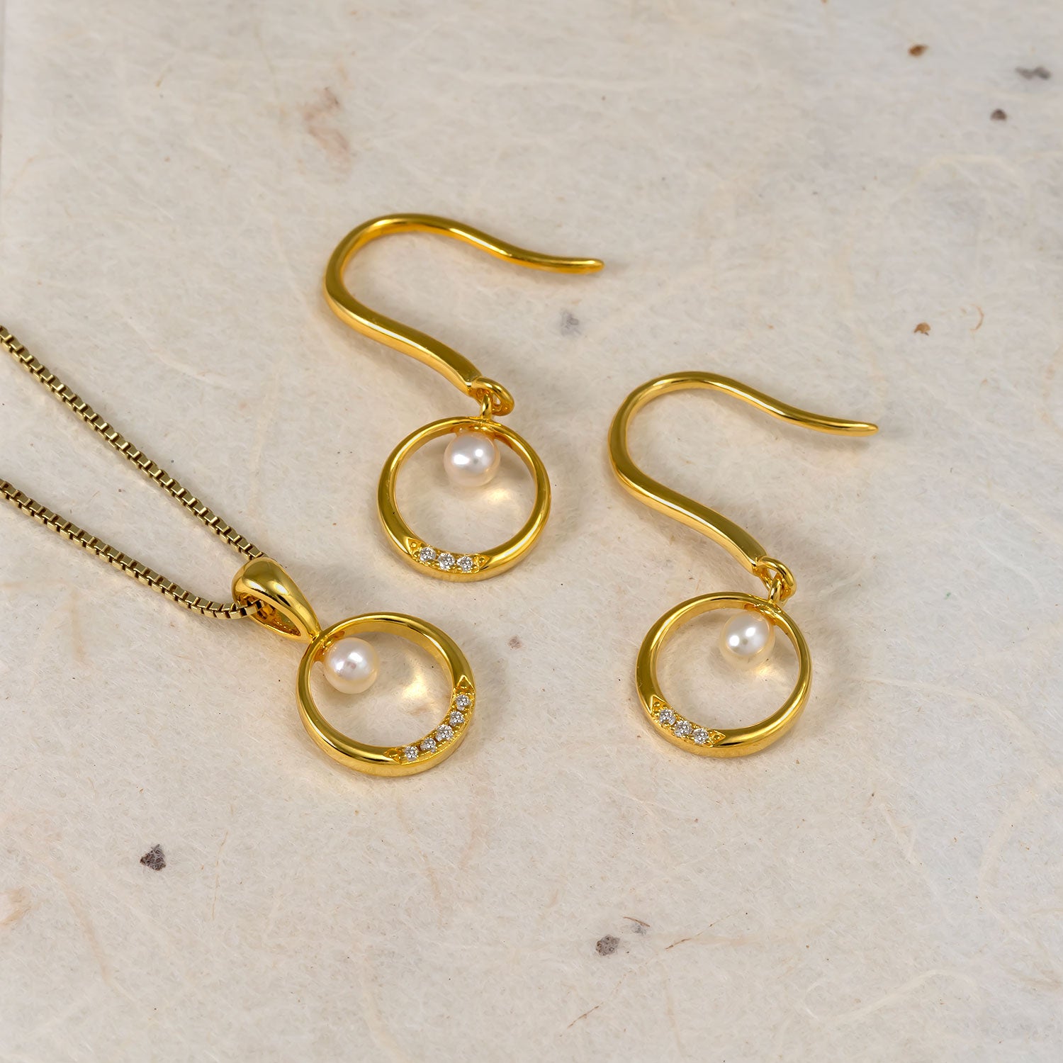 Set of gold vermeil drop earrings and matching pendant featuring delicate freshwater pearls nestled within polished circular frames accented with small lab-grown diamonds.