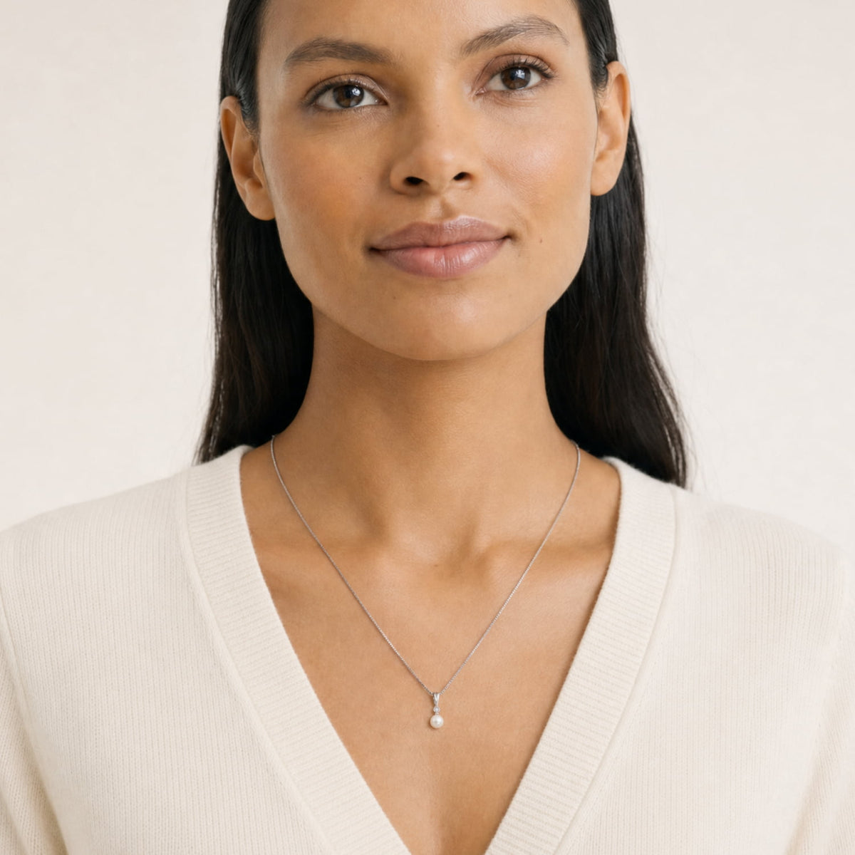Model wears an elegant sterling silver pendant necklace featuring a freshwater pearl drop accented with a small lab grown diamond, suspended from a fine box chain.