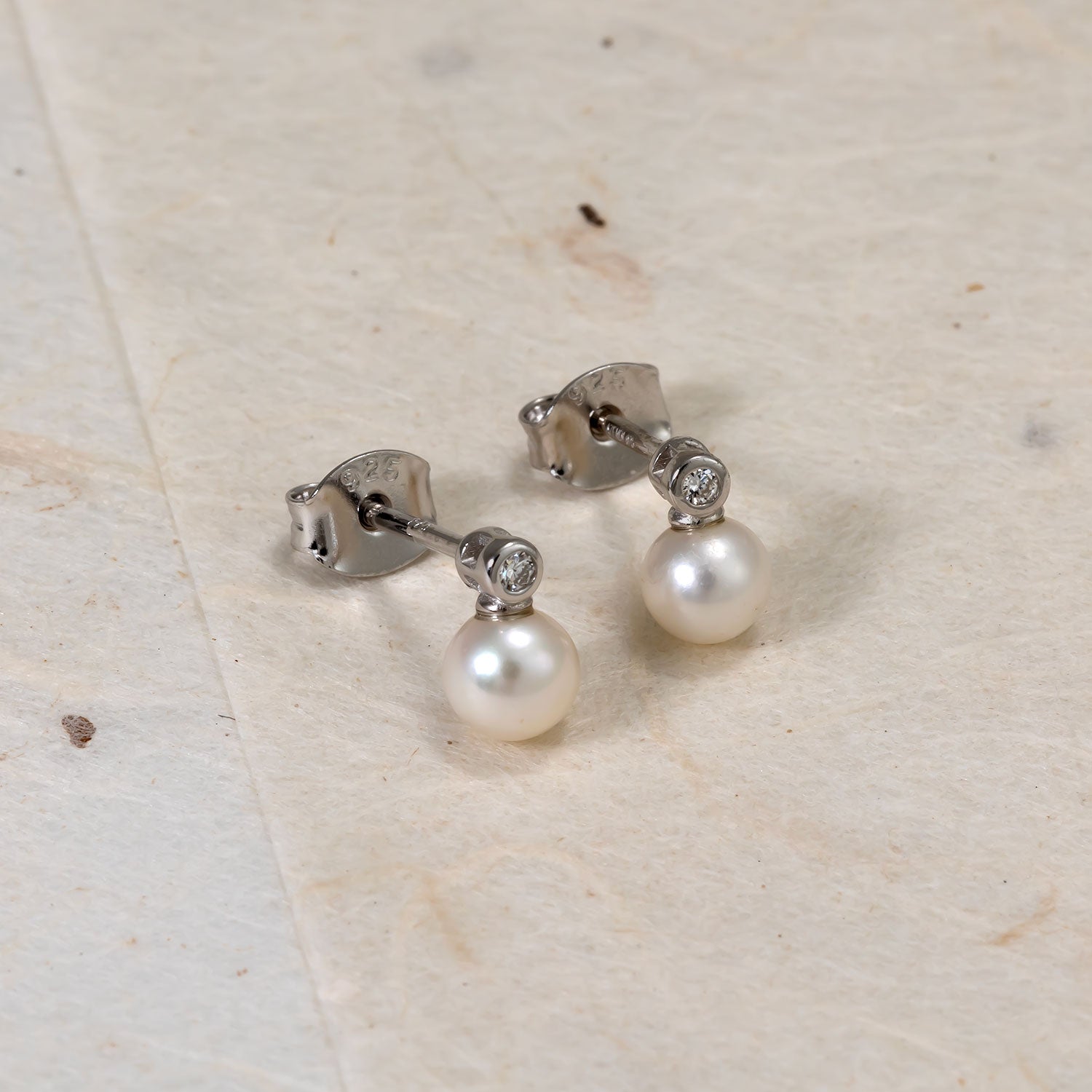 Pair of sterling silver stud earrings featuring freshwater pearls suspended below small lab-grown diamond accents, combining classic elegance with contemporary refinement.