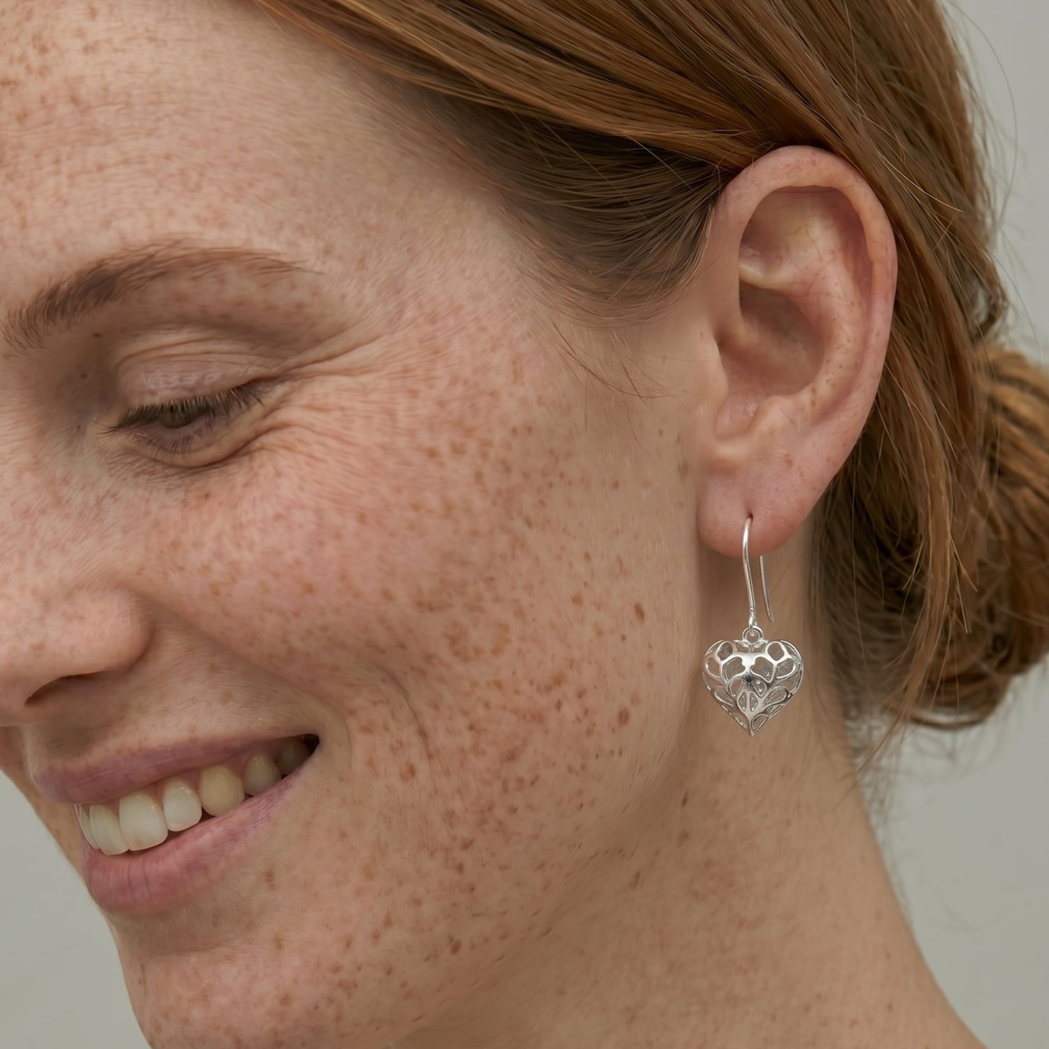 Model wears a pair of sterling silver drop earrings featuring sculptural hanging hearts with delicate openwork inspired by Yorkshire, designed for refined everyday elegance.