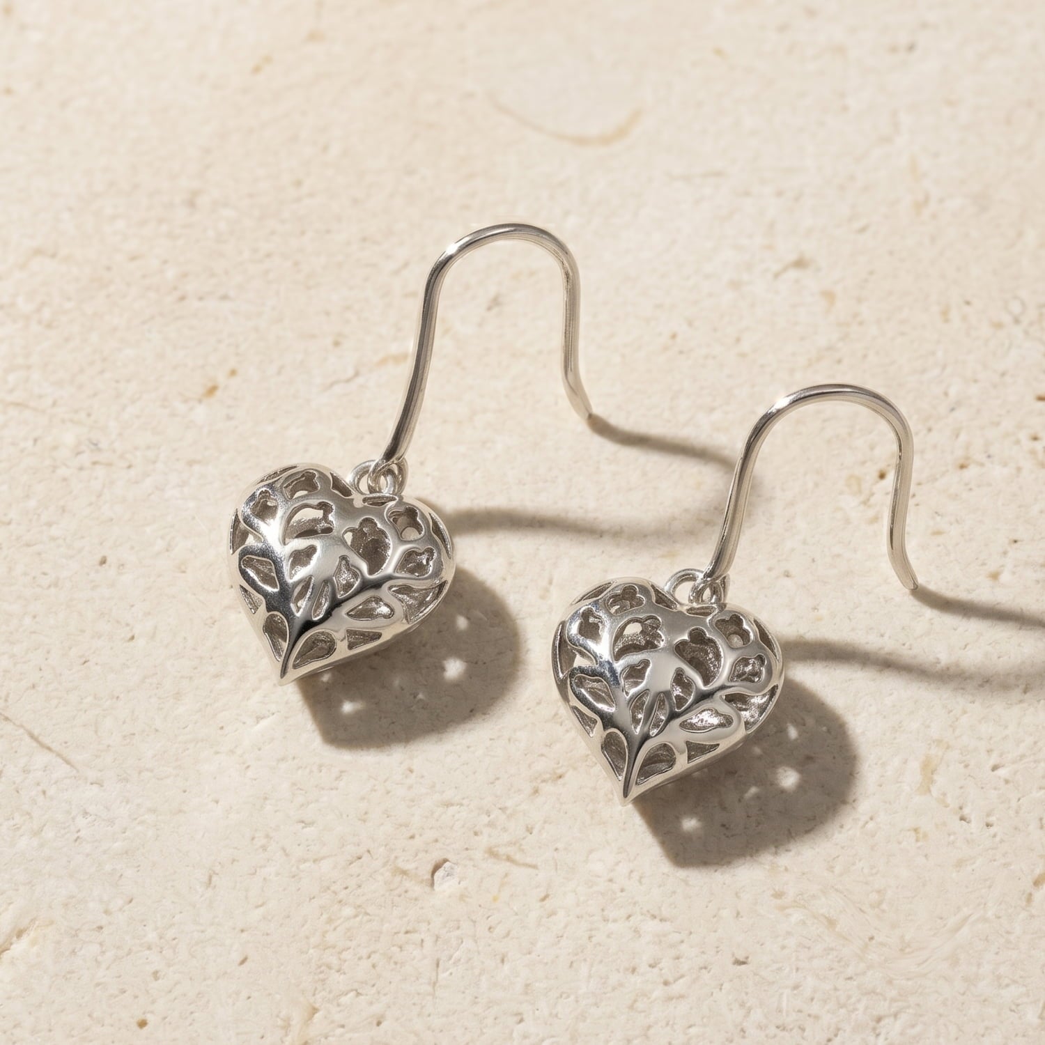 Pair of sterling silver drop earrings featuring sculptural hanging hearts with openwork floral detailing, designed with elegant hooks for comfortable wear.