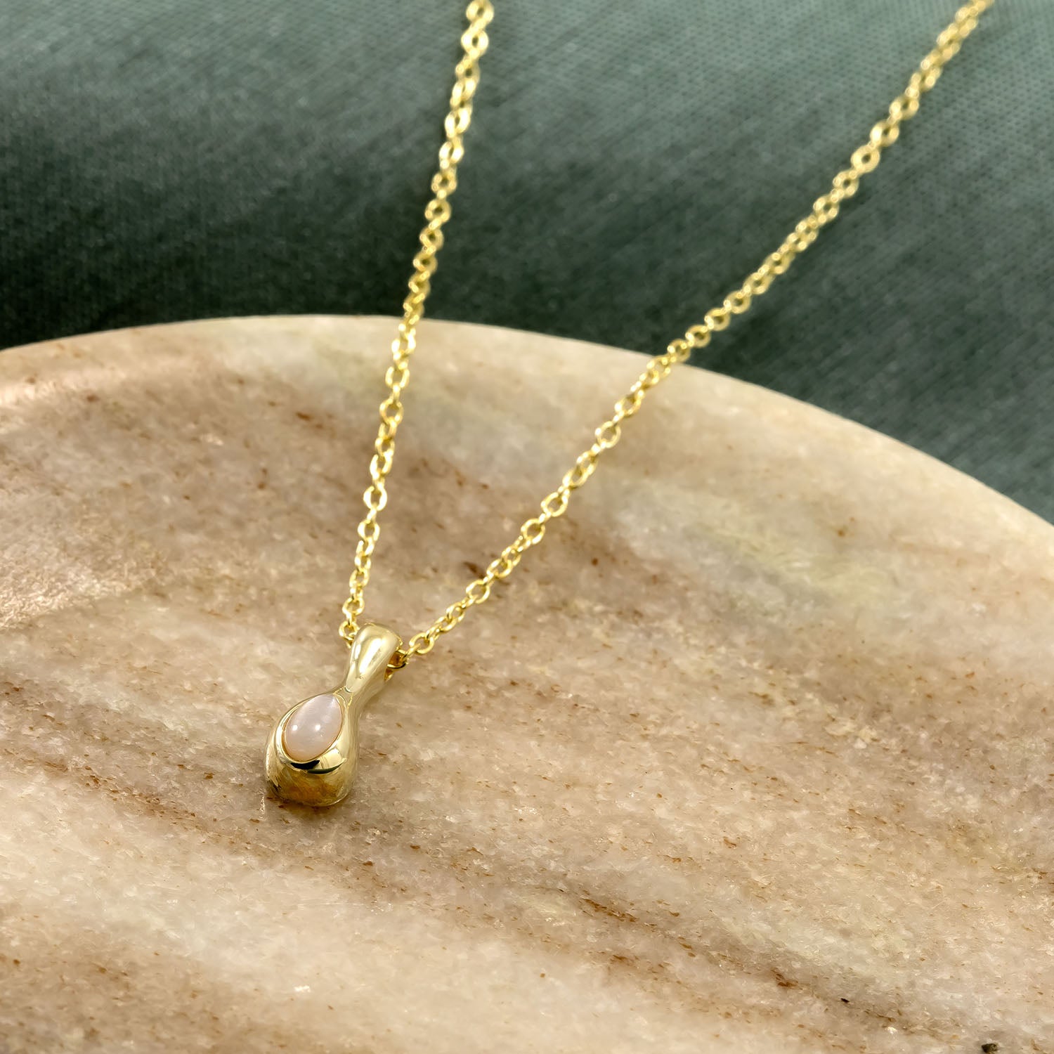 Delicate gold vermeil chain necklace featuring a smooth droplet pendant set with a luminous moonstone, resting on a warm neutral marble surface.