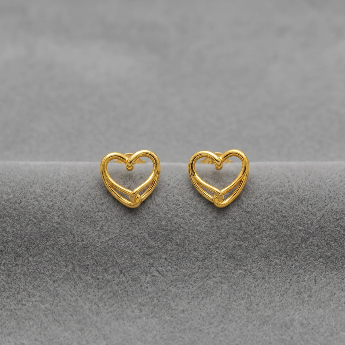 A pair of gold vermeil heart-shaped stud  earrings displayed on a textured gray surface.