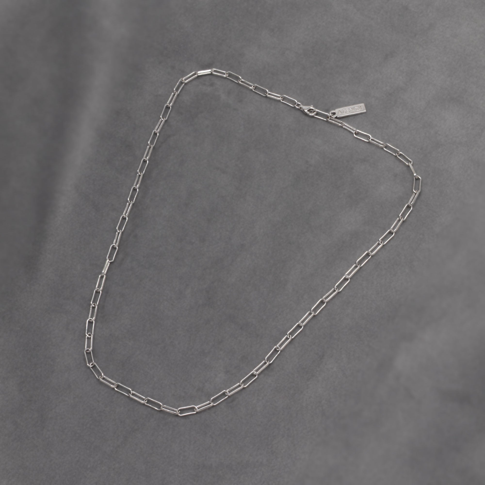 Sterling silver long link paperclip chain necklace with a polished finish and a lobster clasp, highlighting a sleek, contemporary design by Azendi. Placed on a grey velvet cloth.
