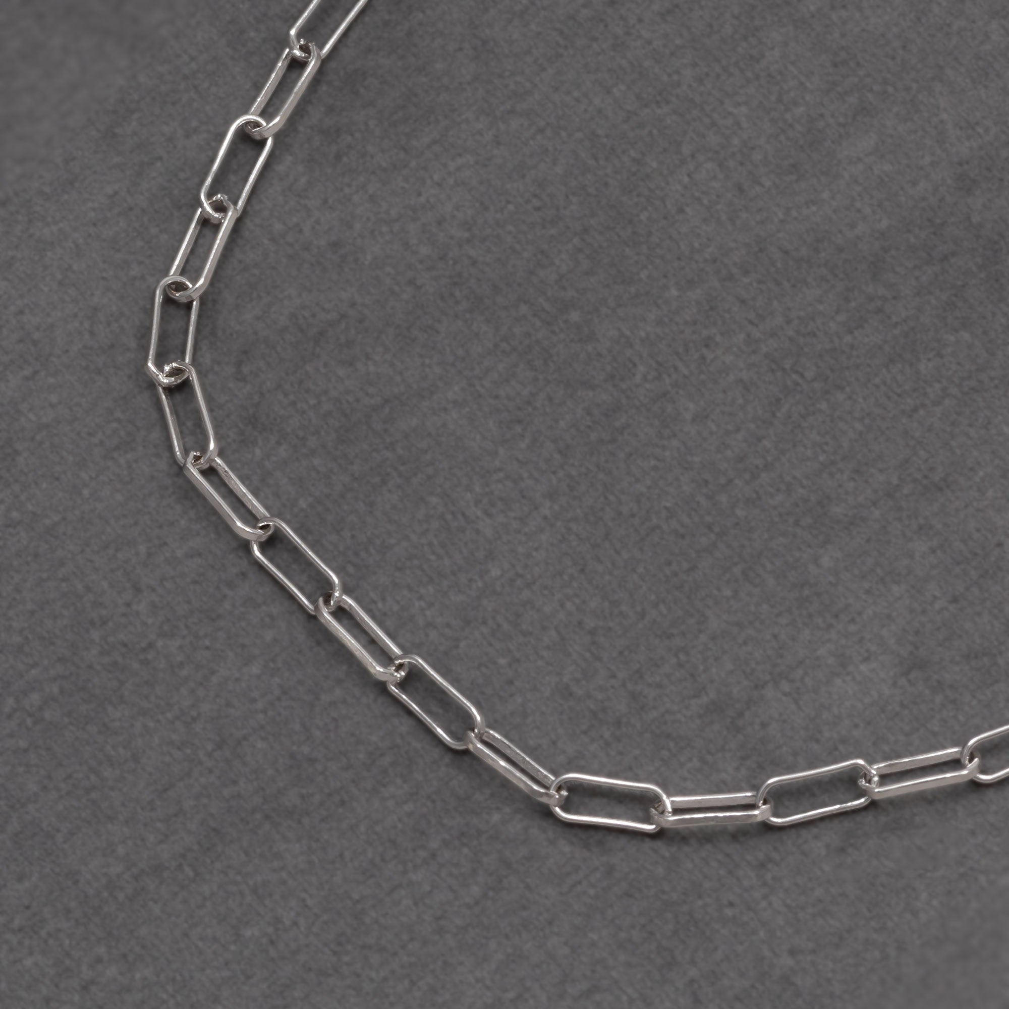 Close up of a sterling silver long link paperclip chain necklace with a polished finish and a lobster clasp, highlighting a sleek, contemporary design by Azendi. Placed on a grey velvet cloth.