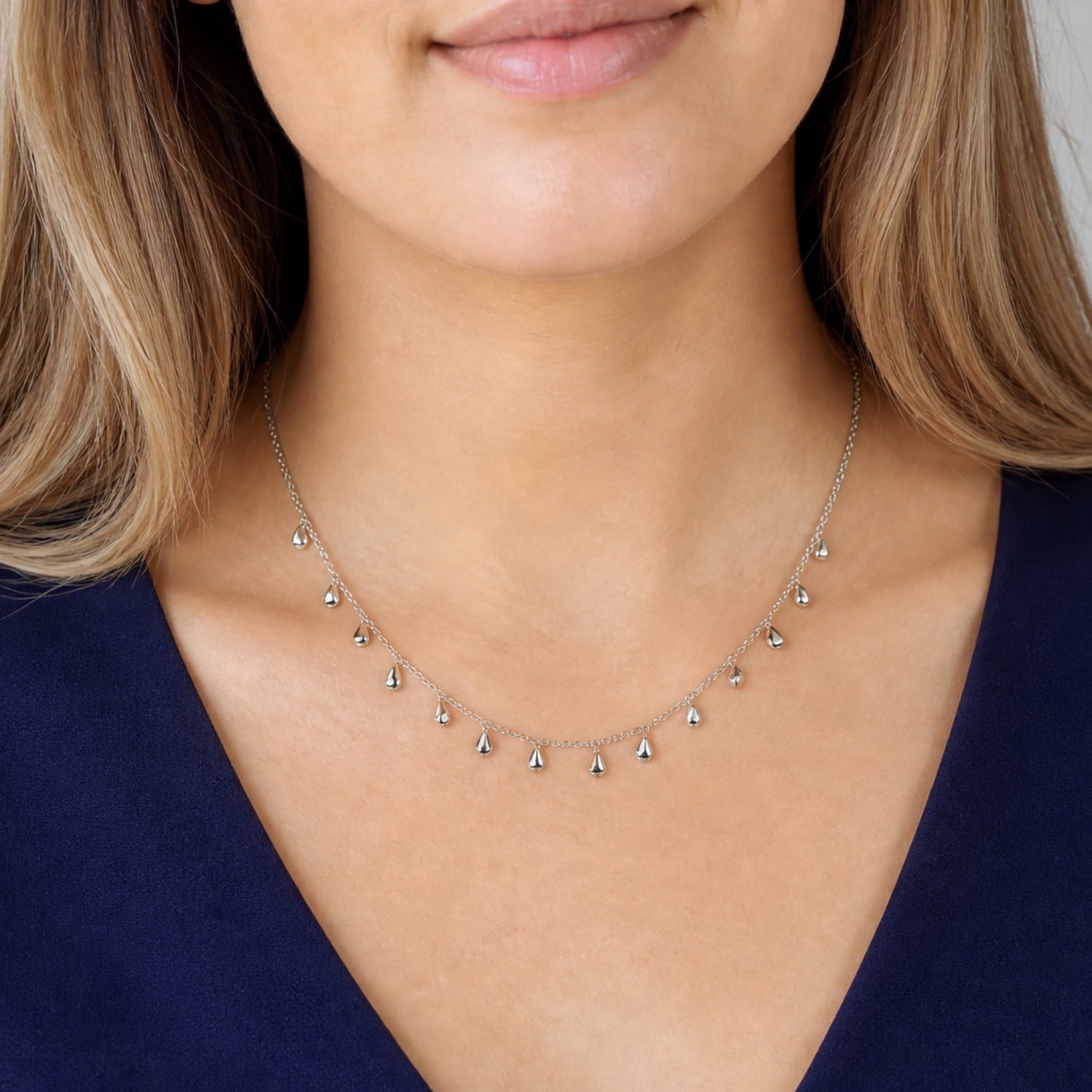 Model wears delicate sterling silver necklace featuring a series of slender, sculptural raindrop-shaped charms suspended from a fine adjustable chain, embodying contemporary elegance.