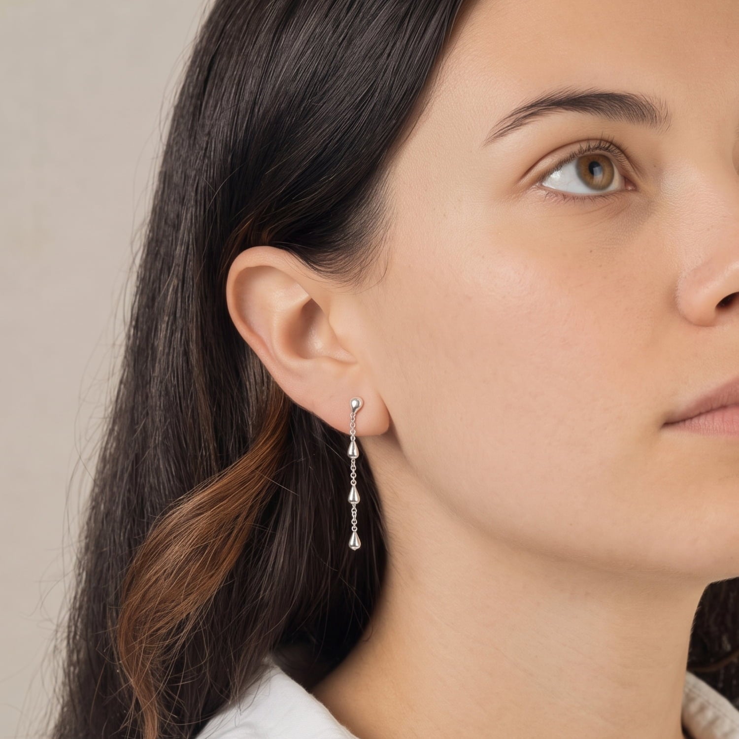 Close-up of a woman wearing sterling silver droplet earrings with a neutral background