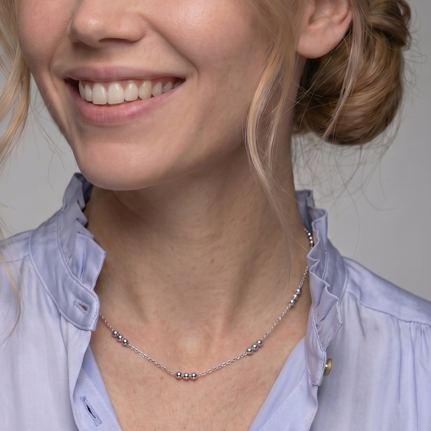 Model wears a sterling silver triple bead chain necklace featuring delicate sterling silver beads spaced along a fine chain with an adjustable extension for versatile wear.