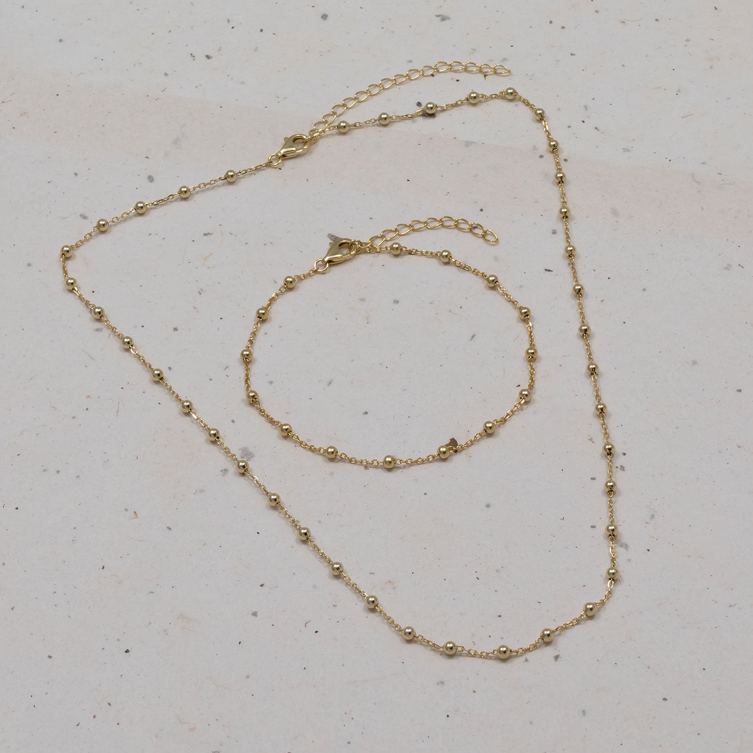 Delicate gold vermeil bead chain bracelet and matching necklace featuring small, polished spherical beads linked by fine chain, displayed against a neutral stone surface.