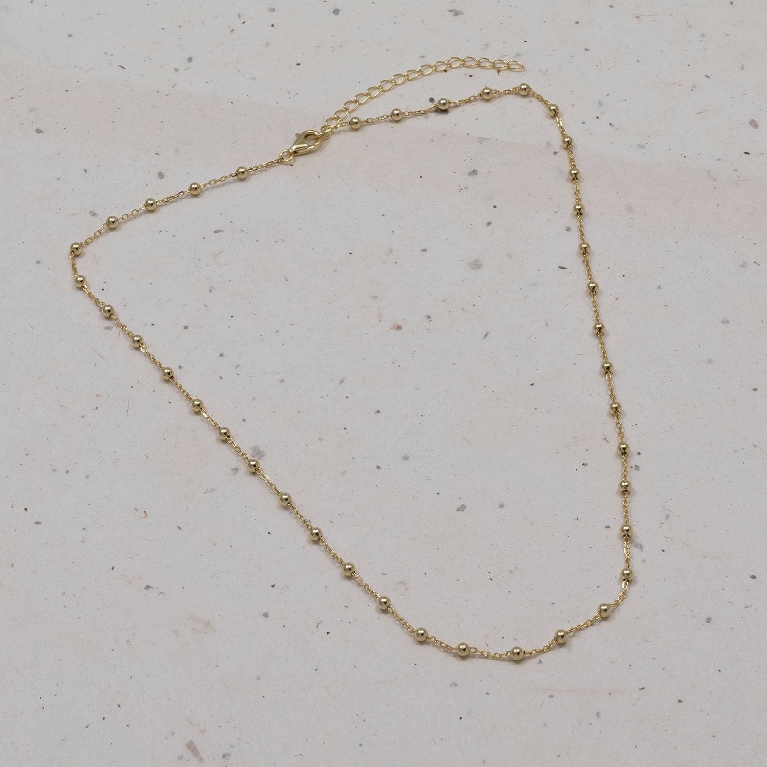 Delicate gold vermeil bead chain necklace featuring small polished spheres along a fine chain, displayed on a neutral stone surface.
