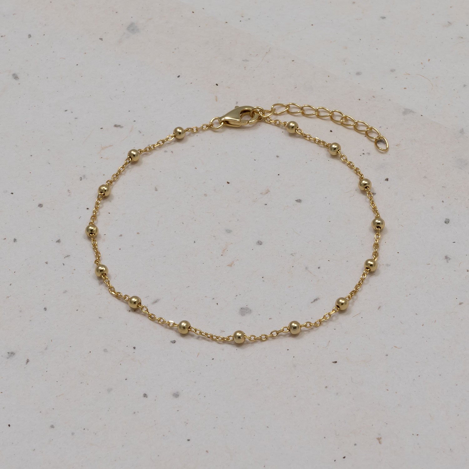 Delicate gold vermeil bracelet featuring a fine chain interspersed with small polished bead accents and an adjustable extension clasp, displayed on a neutral stone surface.