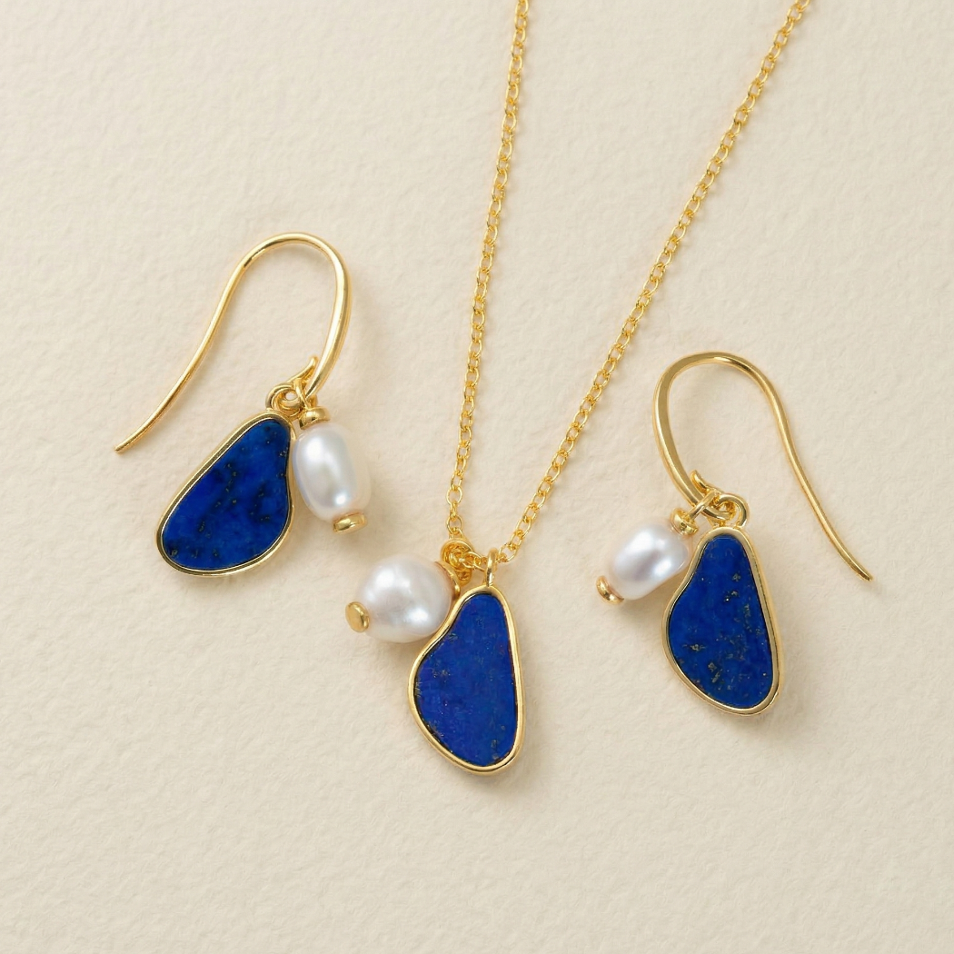 Gold vermeil drop earrings and matching pendant featuring irregular baroque pearls paired with deep blue lapis stones, displayed on a soft neutral background.