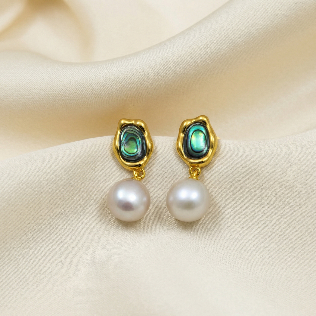 Pair of gold vermeil drop earrings featuring sculptural abalone shells topped with round white pearls, displayed on soft cream satin for a refined look.