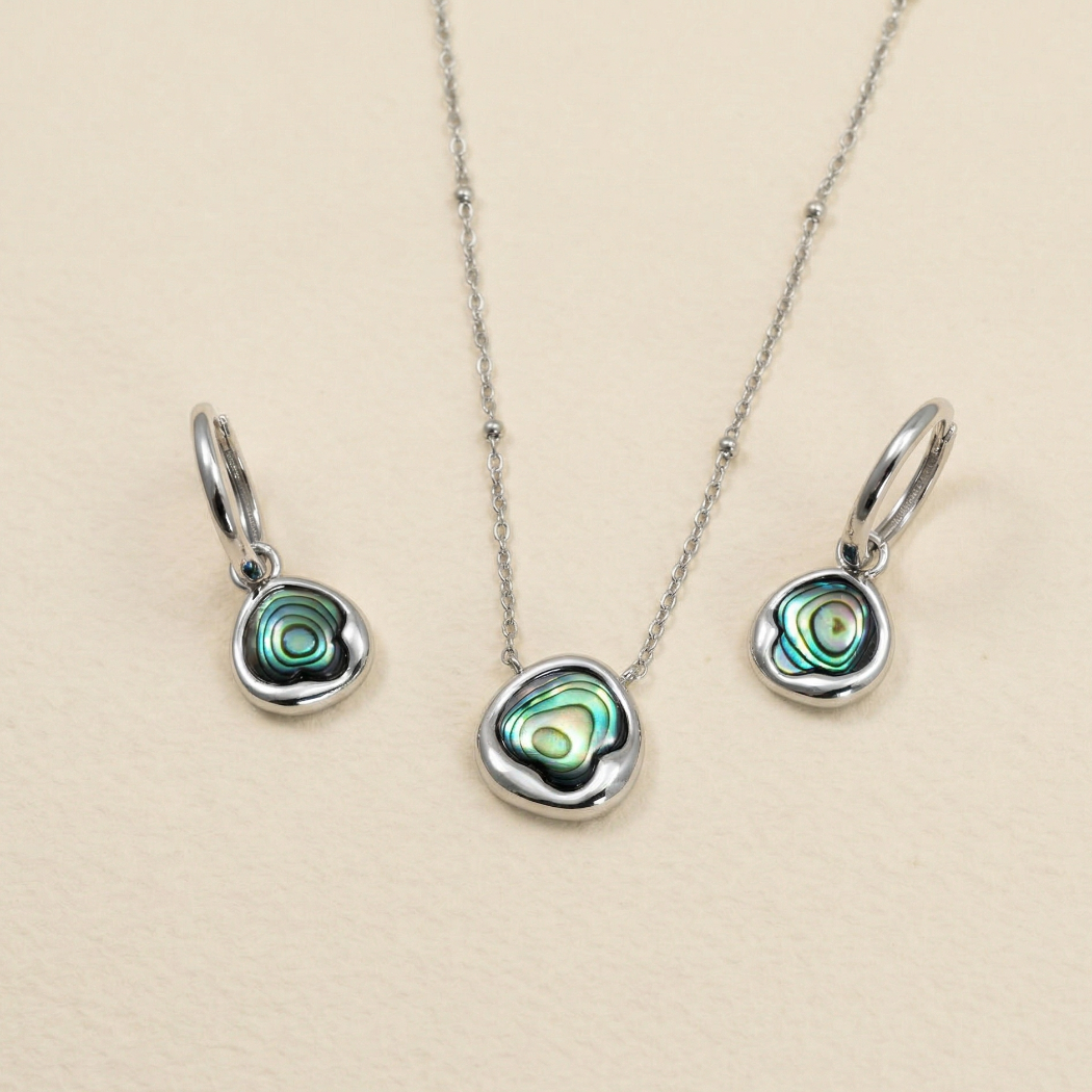 Set of sterling silver hoop earrings and matching necklace featuring organic-shaped abalone shell charms with iridescent green and blue tones, displayed on a neutral background.