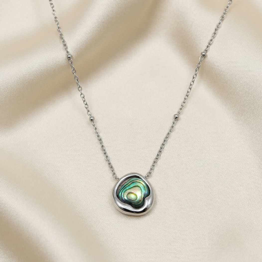 Sterling silver necklace featuring a sculptural pendant with a polished abalone shell center, displayed against a soft cream fabric backdrop.