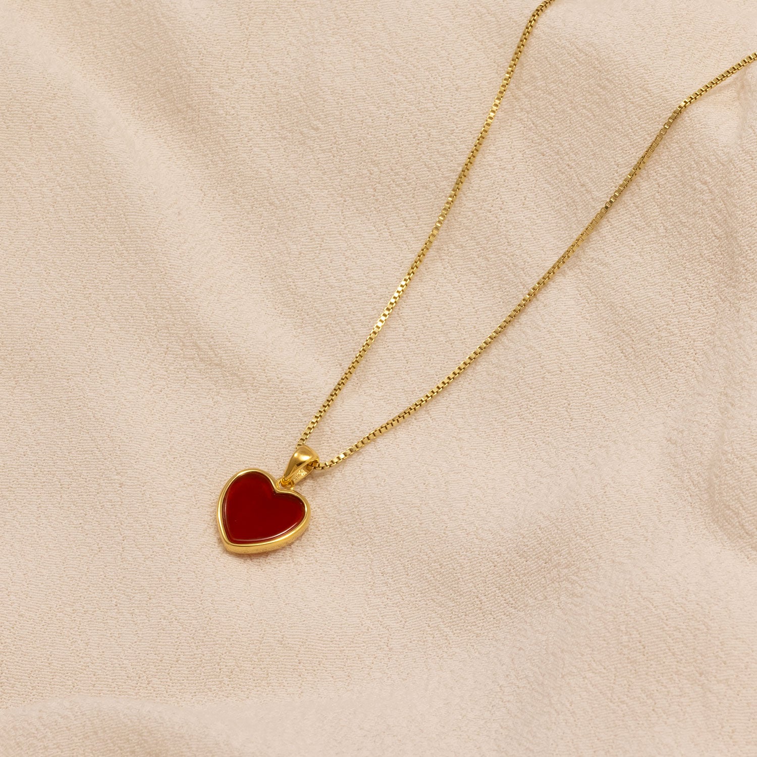 Gold vermeil necklace featuring a heart-shaped red agate pendant with a smooth polished finish, displayed on a soft beige fabric backdrop.