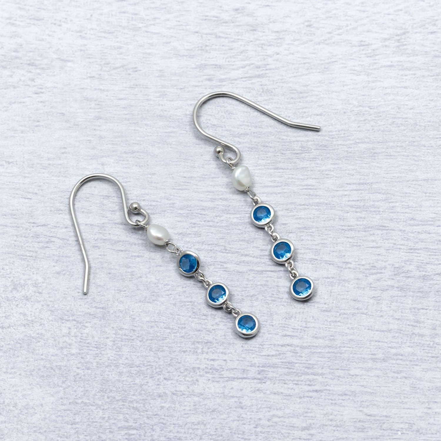 Sterling silver drop earrings featuring freshwater pearls paired with bezel-set blue cubic zirconia stones, designed with a refined and elegant contemporary style.