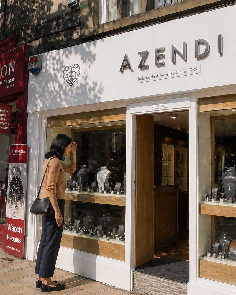 Woman in a tan top and black pants peering into a jewellery display window filled with sterling silver pieces outside an Azendi boutique on a sunny day.