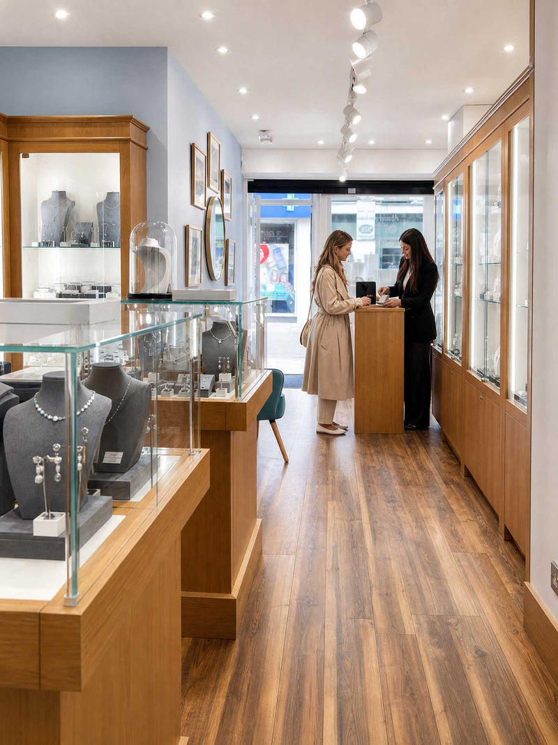 Interior of a bright jewellery boutique featuring wooden floors and display cases with sterling silver pieces, with two women conversing near the front window.