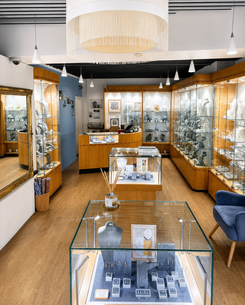 A bright, contemporary jewellery showroom with wooden display cabinets filled with silver jewellery pieces, glass cases showcasing necklaces and rings, and modern pendant lighting.