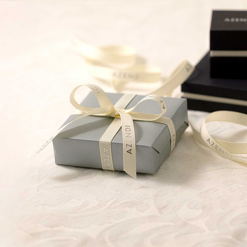 Silver gift box with a cream ribbon on a light surface, branded 'AZENDI'.