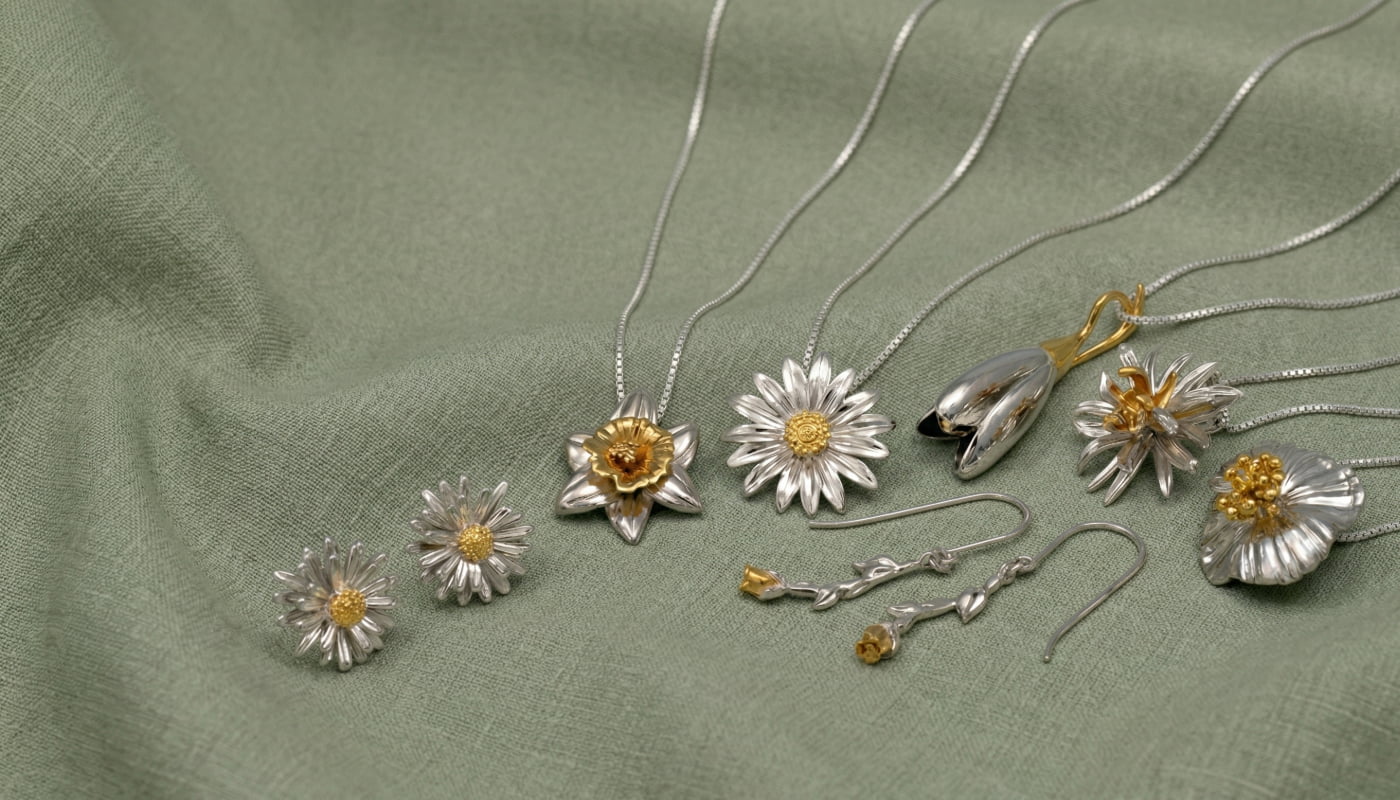 Various silver and gold vermeil flower-themed jewelry pieces including necklaces, earrings, and pendants arranged on a green fabric background.