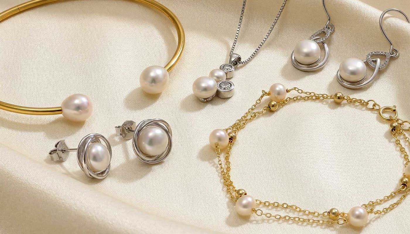 Collection of elegant sterling silver and gold vermeil jewellery featuring pearls, including a bangle, earrings, necklaces, and a delicate bracelet arranged on a soft cream fabric.