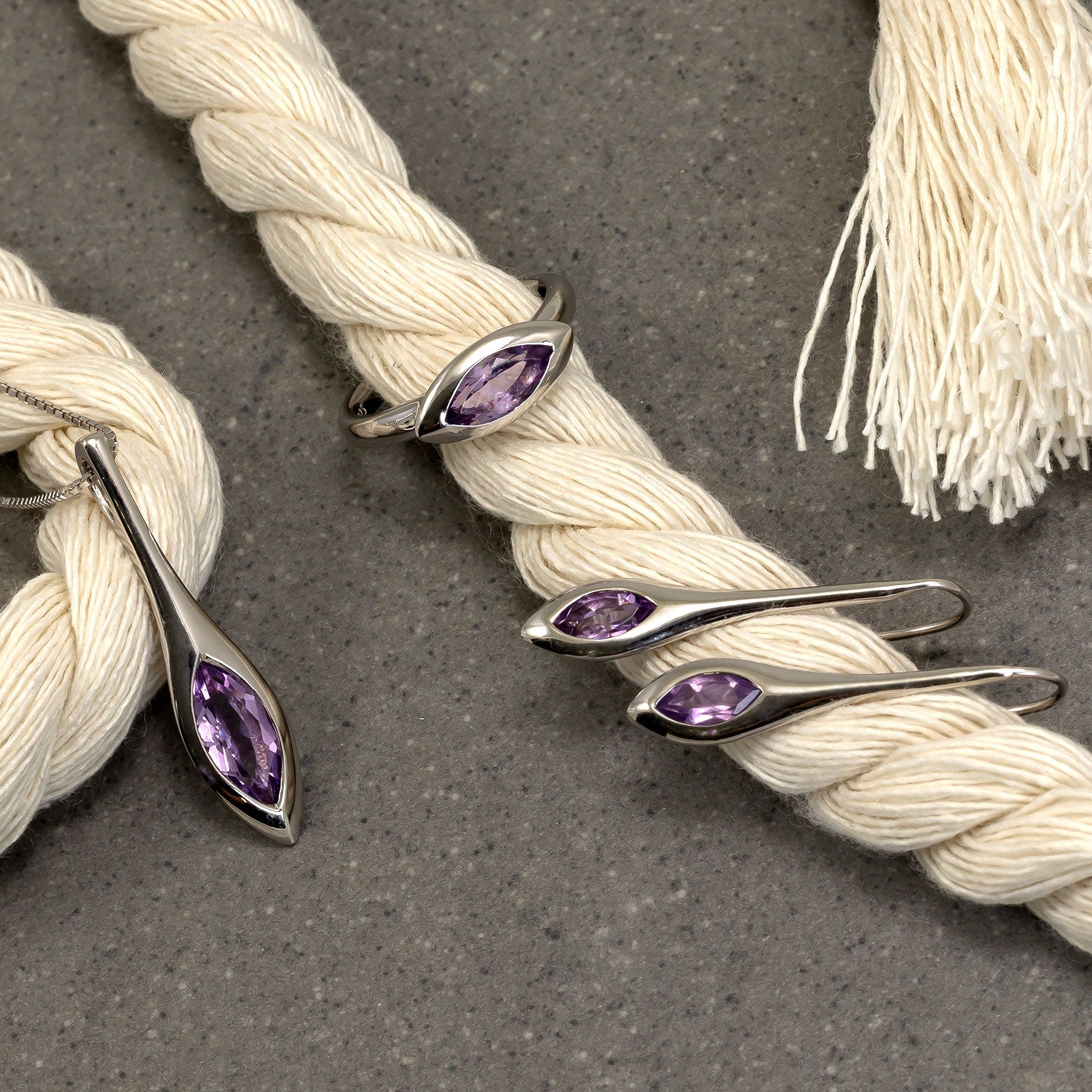 Sterling silver jewellery set featuring elongated marquise-cut amethyst stones in a sleek, sculptural design displayed on natural textured rope against a grey background.