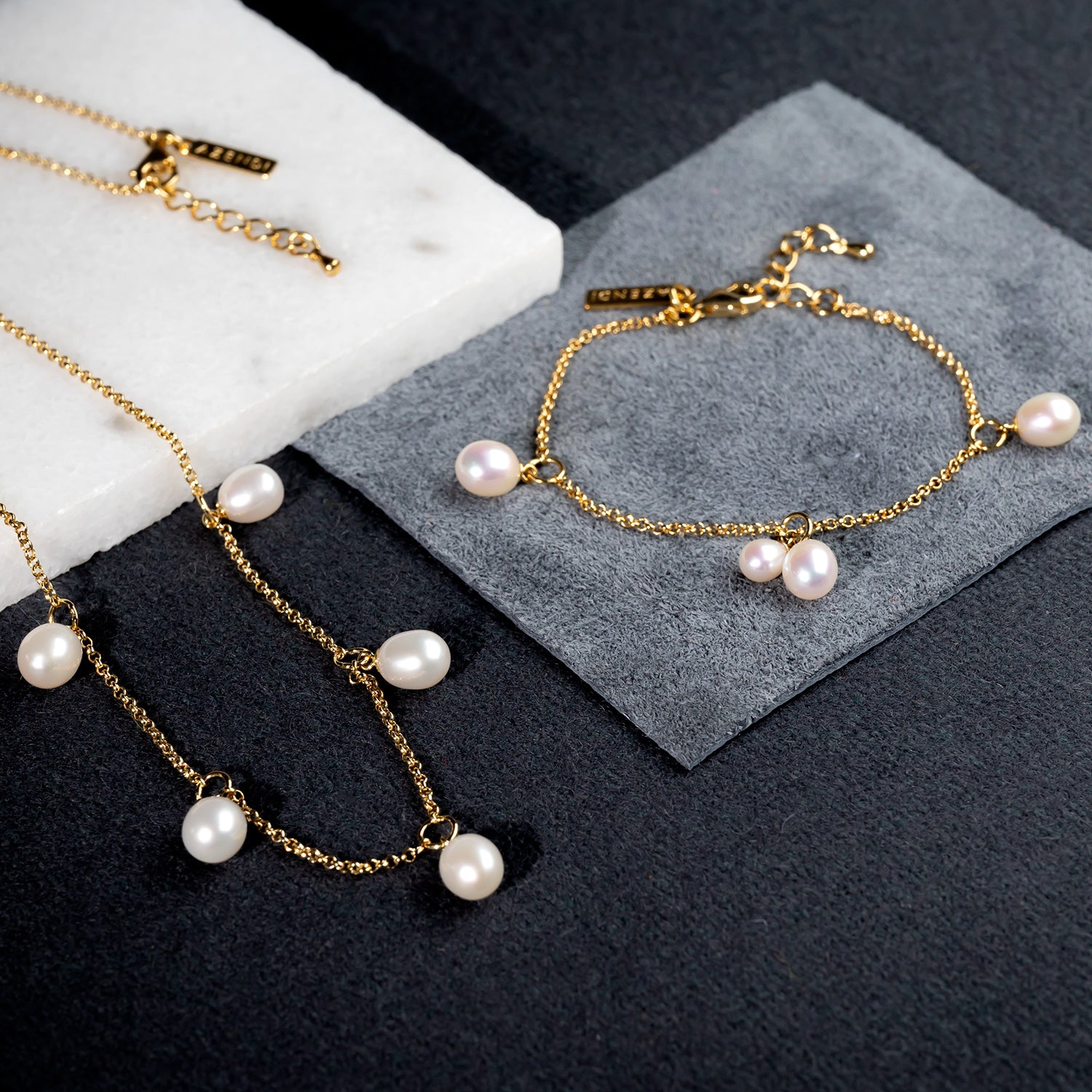 Delicate gold vermeil necklace and matching bracelet set featuring teardrop freshwater pearls on fine chains, presented on black and grey textured surfaces.