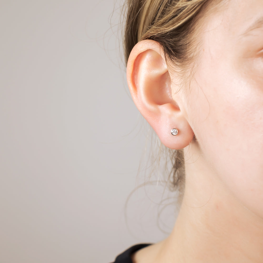 Close-up of a single sterling silver stud earring featuring a 3mm clear brilliant cut stone, worn on the earlobe against a soft neutral background.