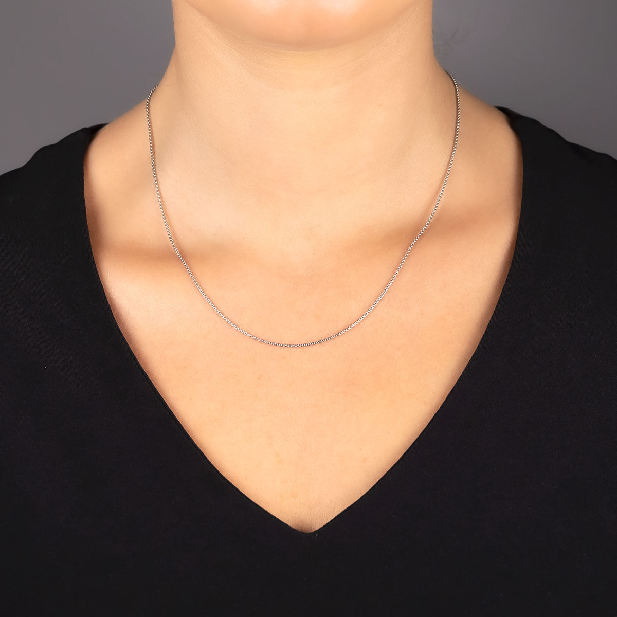 Close-up of a person wearing a delicate sterling silver rollo chain necklace with a sliding adjuster, styled with a black V-neck top against a neutral background.