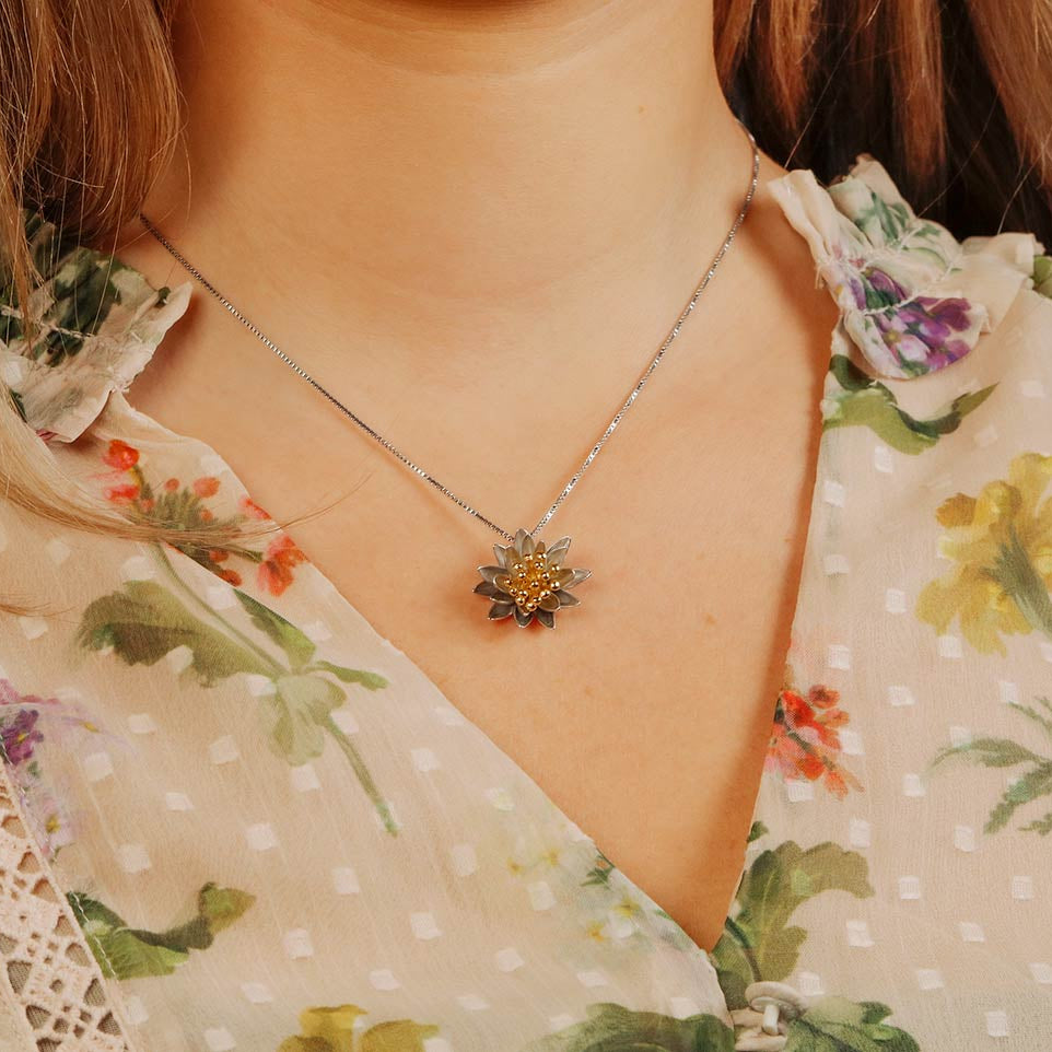 Sterling silver pendant inspired by a water lily flower with detailed petals and a gold vermeil center, worn on a fine chain for a delicate, elegant look.