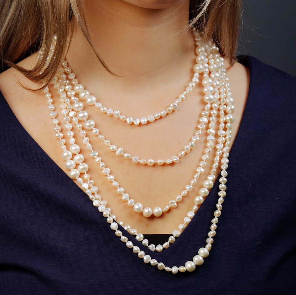 Multiple pearl necklace layered on a person wearing a dark blue top.