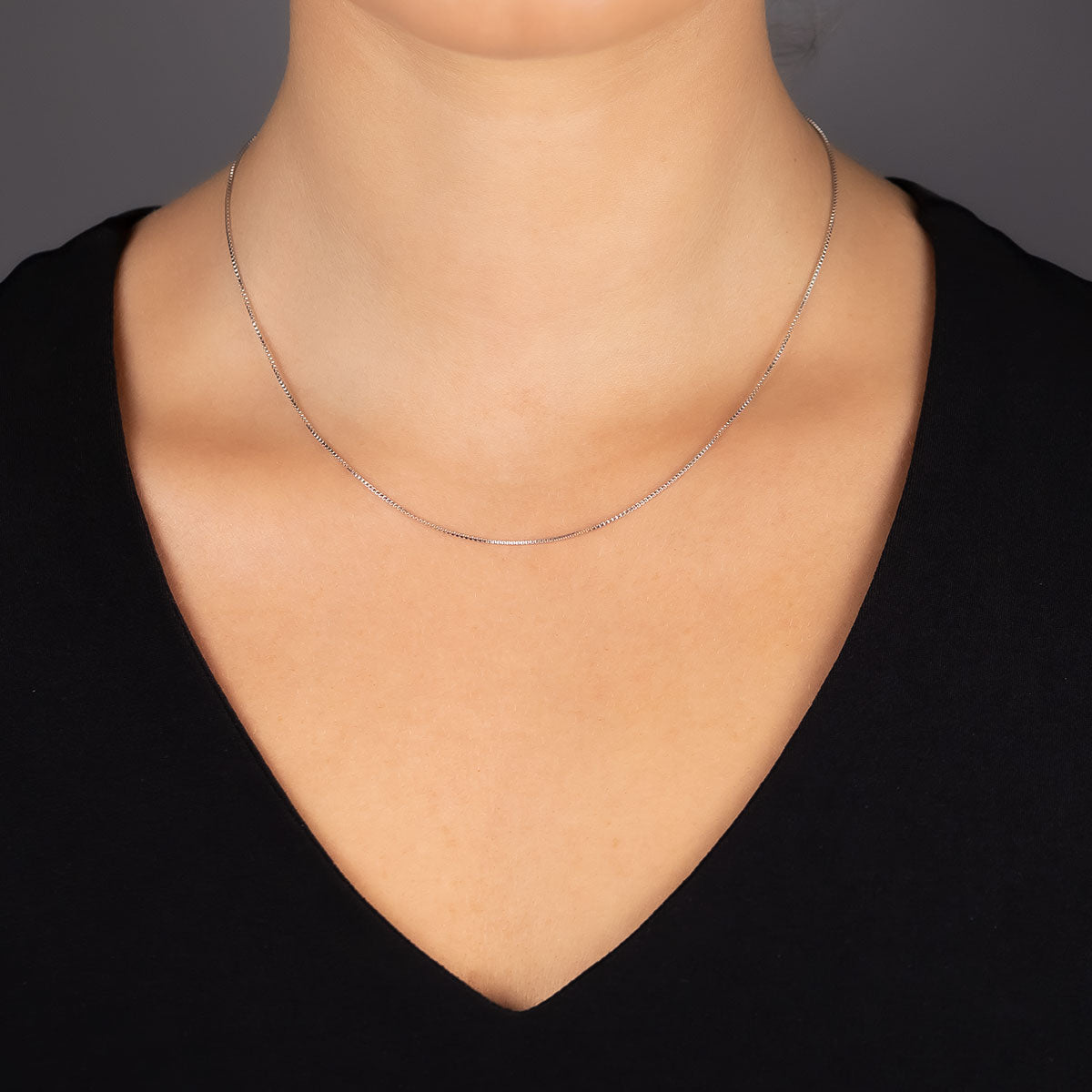 Delicate sterling silver box chain necklace with an adjustable length, gently resting on the neckline of a black V-neck top against a neutral background.