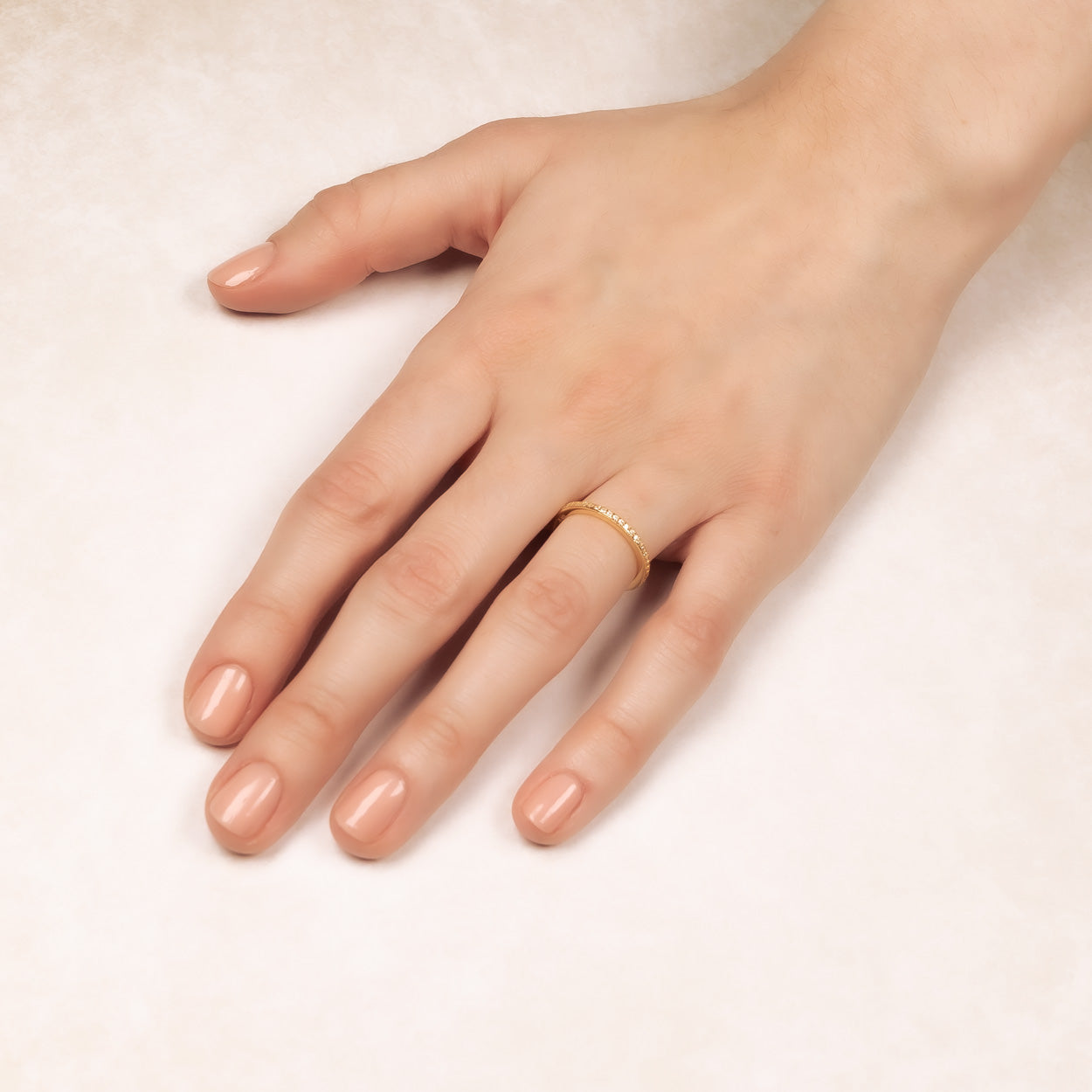 Hand with neutral-toned manicured nails wearing a slender gold vermeil pavé eternity ring on the ring finger, resting on a soft cream background.