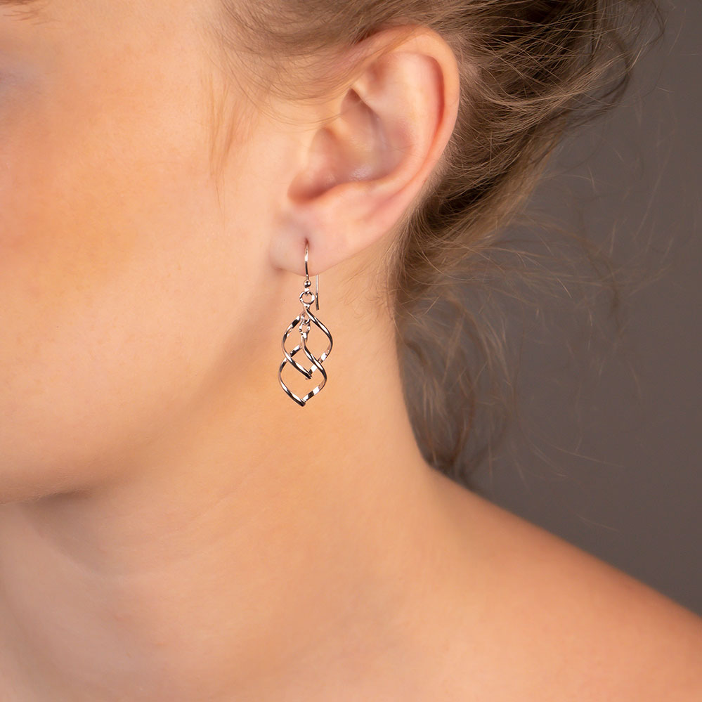 Close-up of a woman's ear wearing Spiral Waves Drop Earrings - Silver, showcasing delicate, flowing wave-shaped silver jewellery approximately 4cm in length.