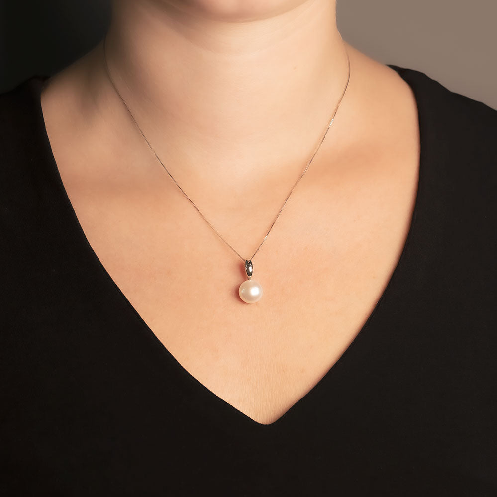 Delicate 9 carat white gold necklace featuring a single freshwater pearl drop pendant suspended from a fine chain, styled with a classic black V-neck top.