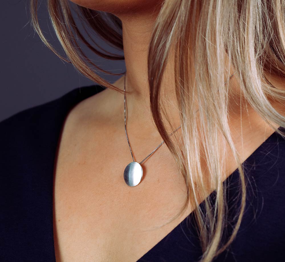Sleek sterling silver pendant featuring a smooth satin finish in a rounded button shape, suspended from a fine chain for a modern and elegant look.