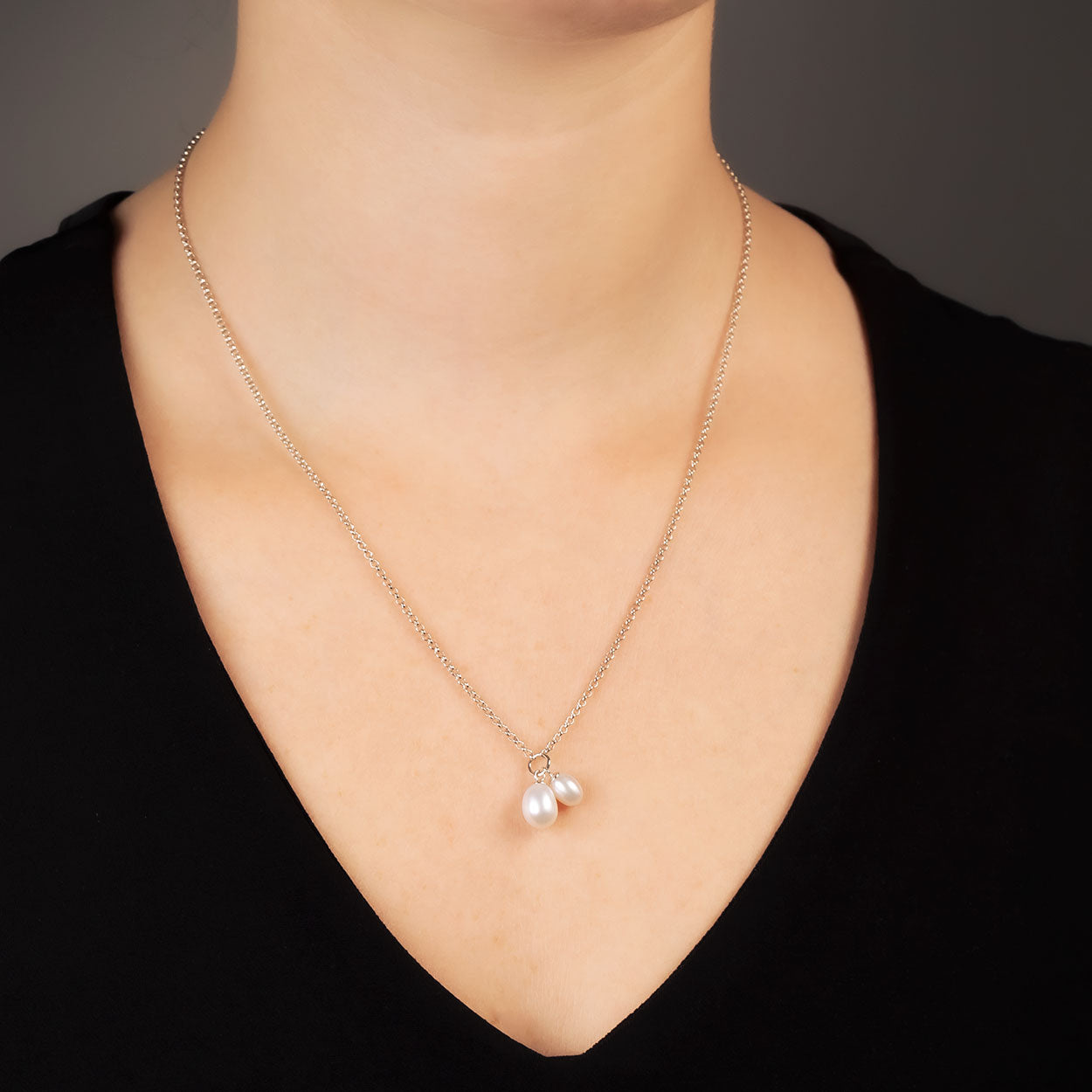 Sterling silver necklace featuring a delicate chain with two teardrop freshwater pearl pendants, styled on a model wearing a black top against a dark background.