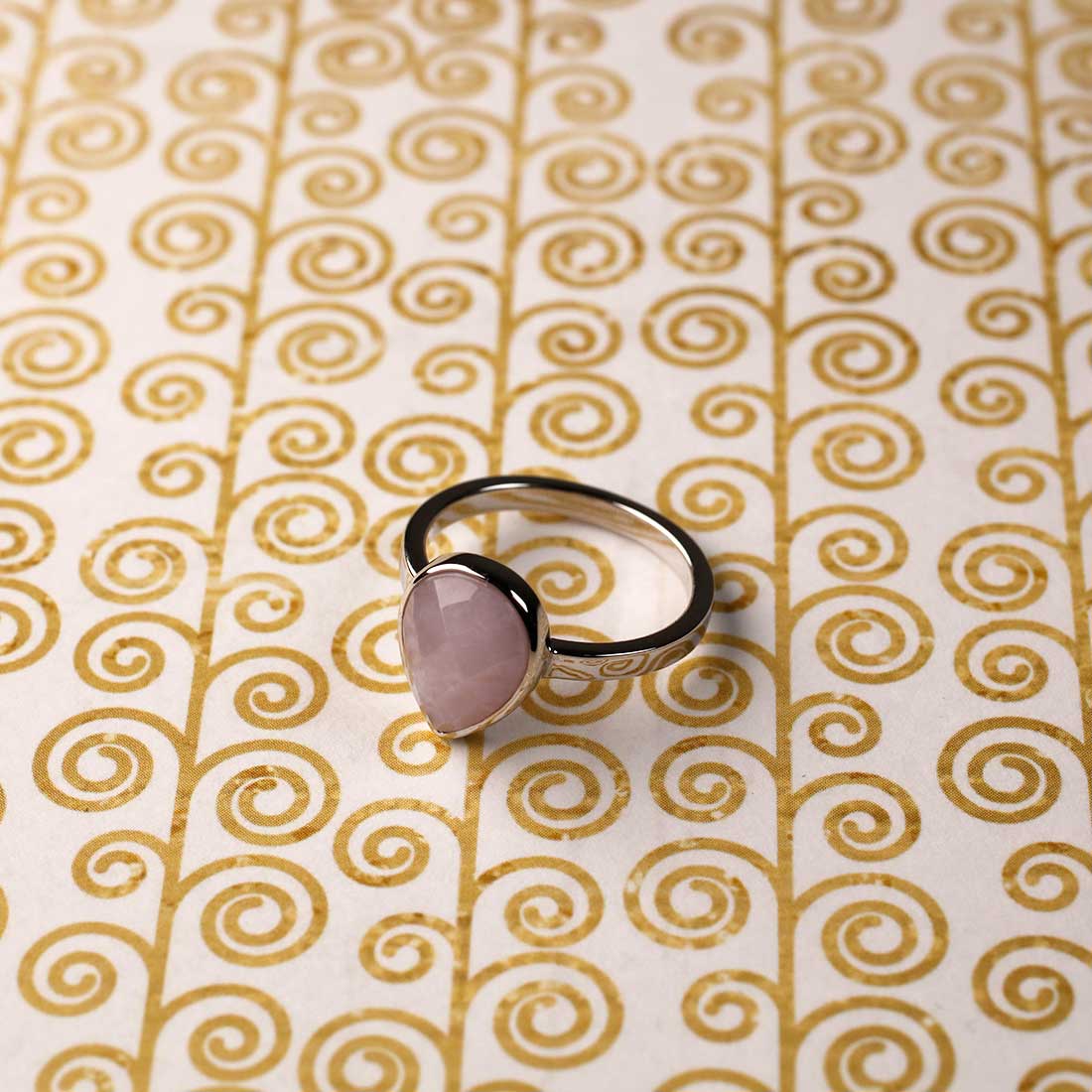 Sterling silver ring featuring a teardrop-shaped amethyst stone with a smooth bezel setting, showcasing elegant sculptural design on a gold swirl patterned background.