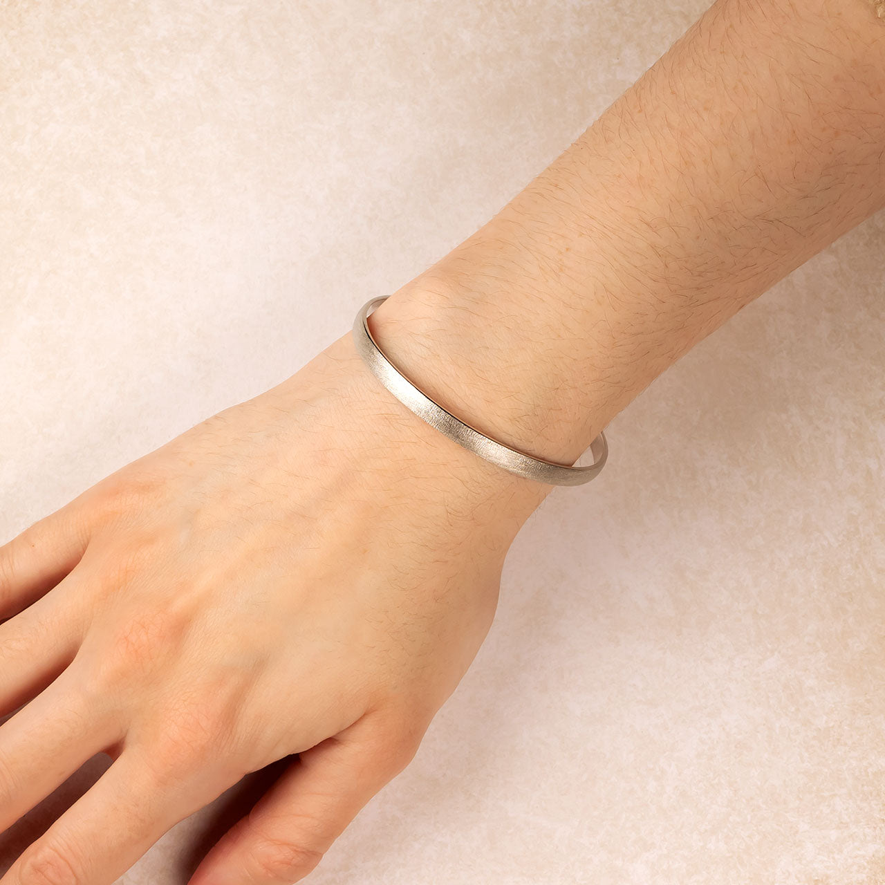 Sterling silver bangle with a subtle satin finish, elegantly styled on a wrist to highlight its smooth, sculptural design and contemporary craftsmanship by Azendi.