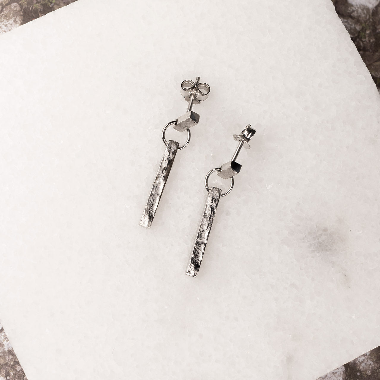 Pair of slender sterling silver drop earrings featuring textured vertical bars suspended from small geometric links, embodying minimalist British silver jewellery design.