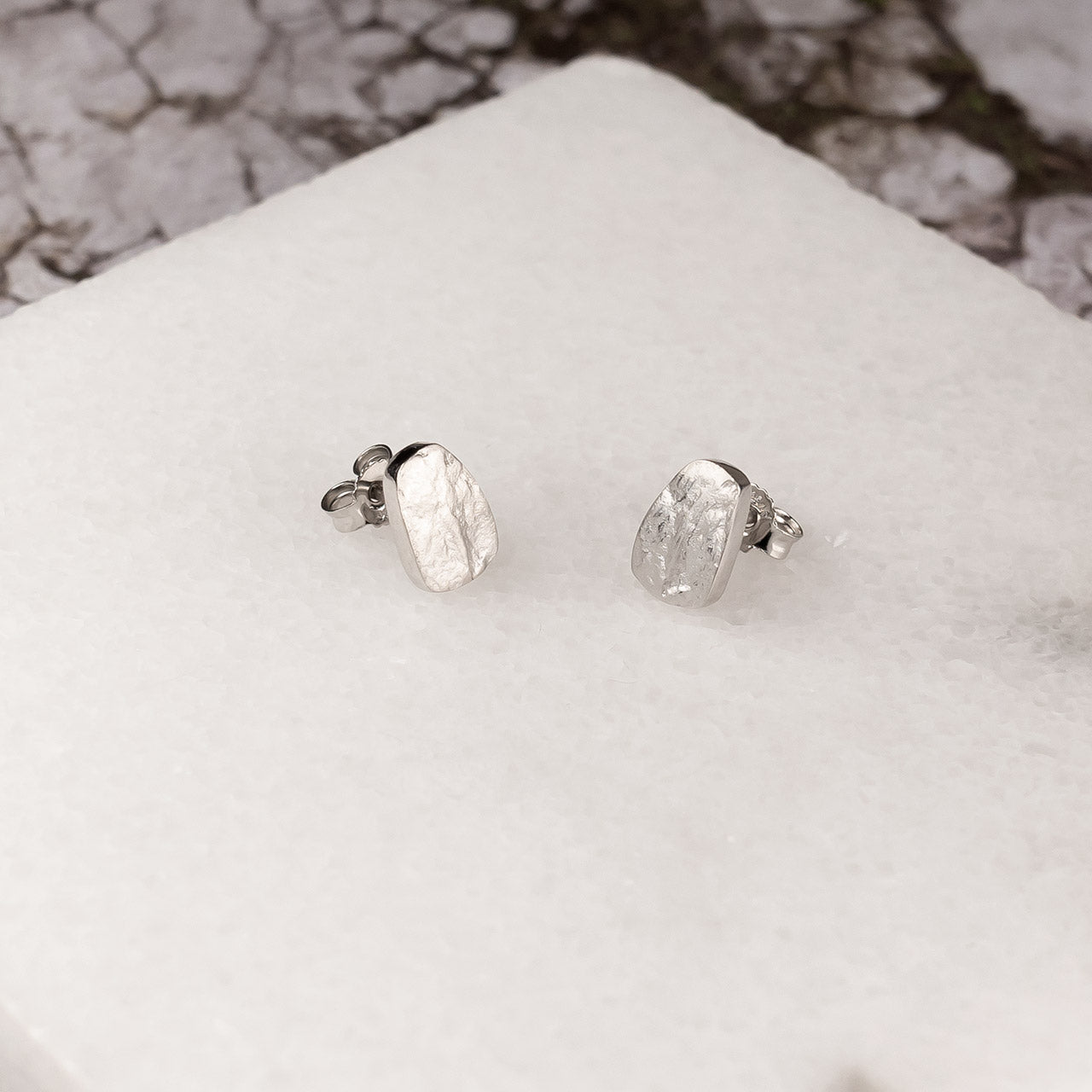 Pair of sterling silver stud earrings inspired by natural pebble shapes, featuring textured surfaces for a subtle, sculptural effect in contemporary silver jewellery.