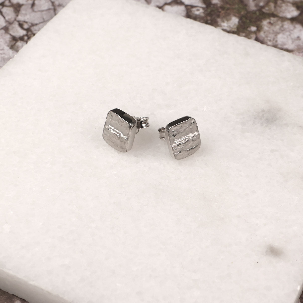 Rectangular sterling silver stud earrings with a subtle hammered texture and a polished linear detail, showcasing contemporary sculptural design in fine silver jewellery.