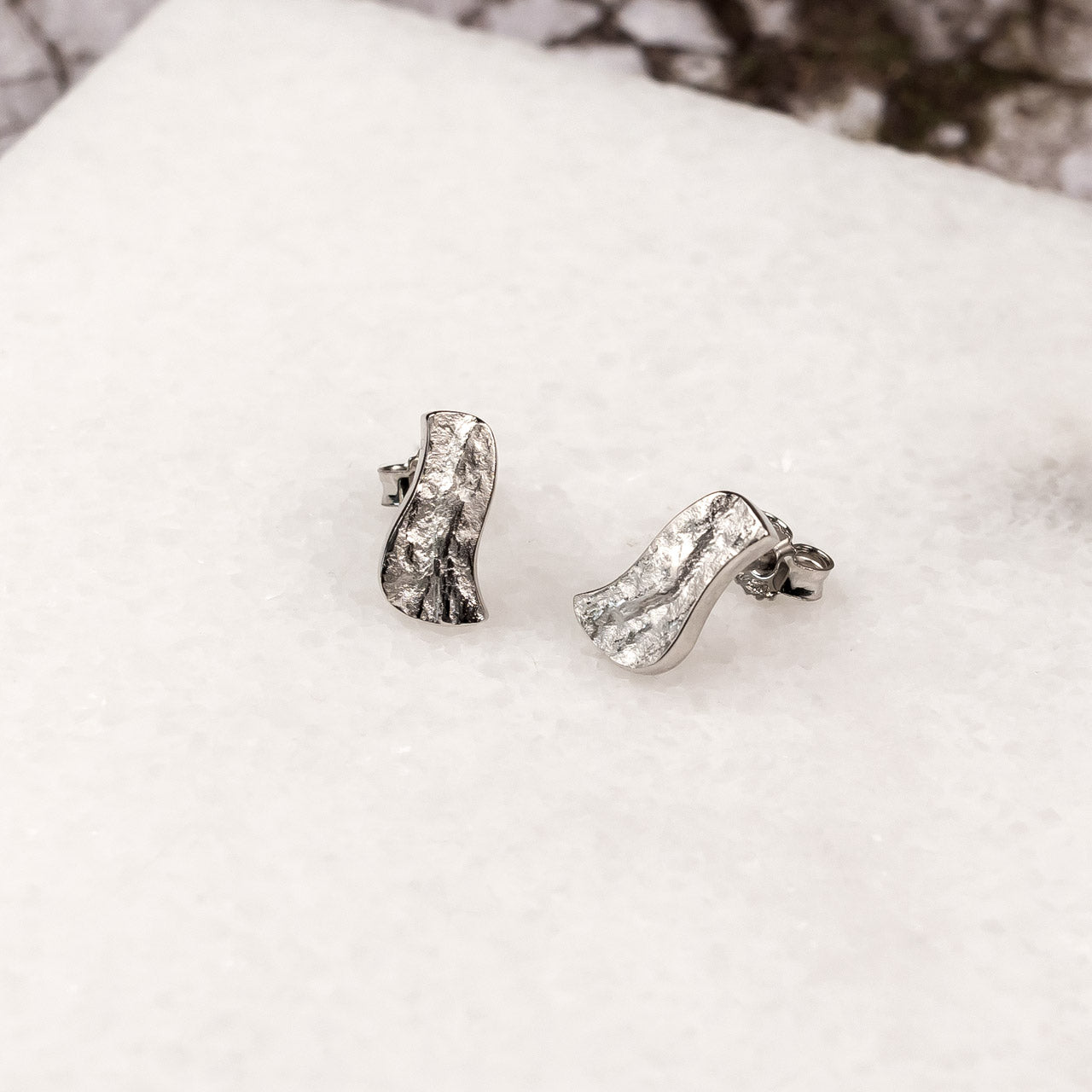 Pair of sterling silver stud earrings featuring an organic, textured wave design inspired by natural formations, embodying refined contemporary silver jewellery.