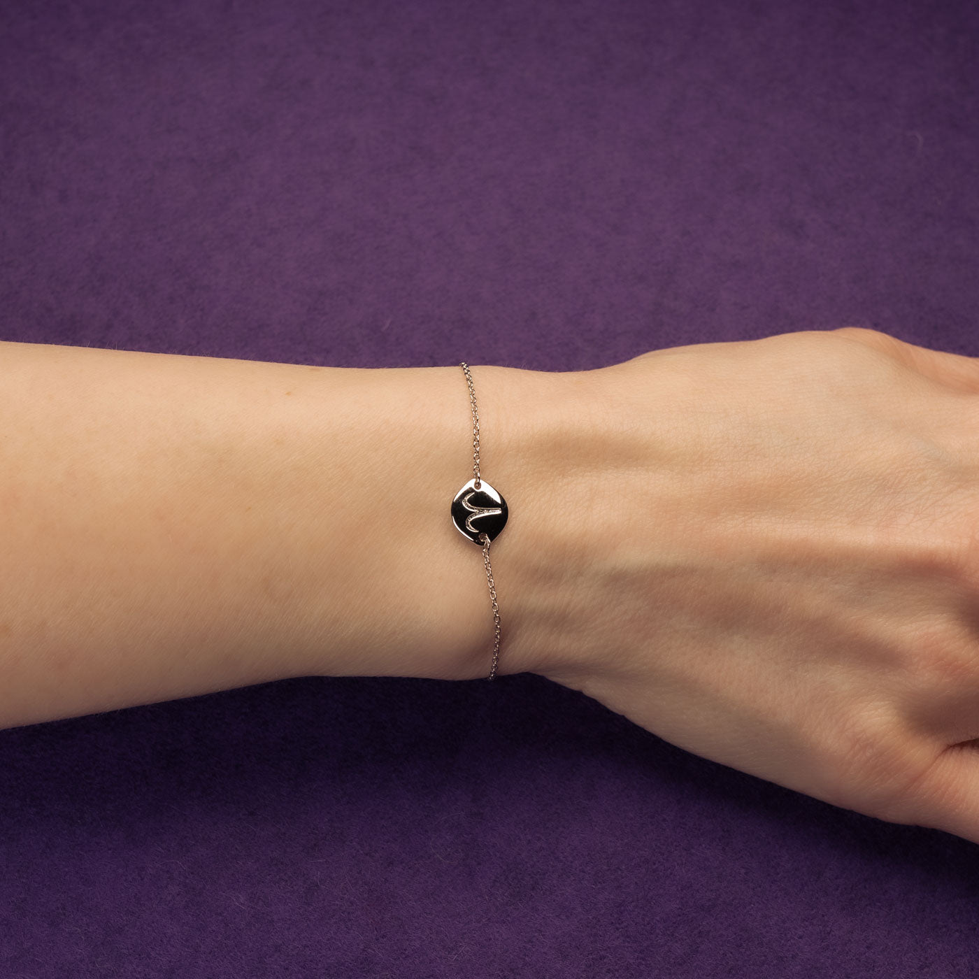 Delicate sterling silver bracelet featuring a sculptural Aries zodiac symbol on a polished disc, with an adjustable sliding bead for a customizable fit, displayed on a wrist.