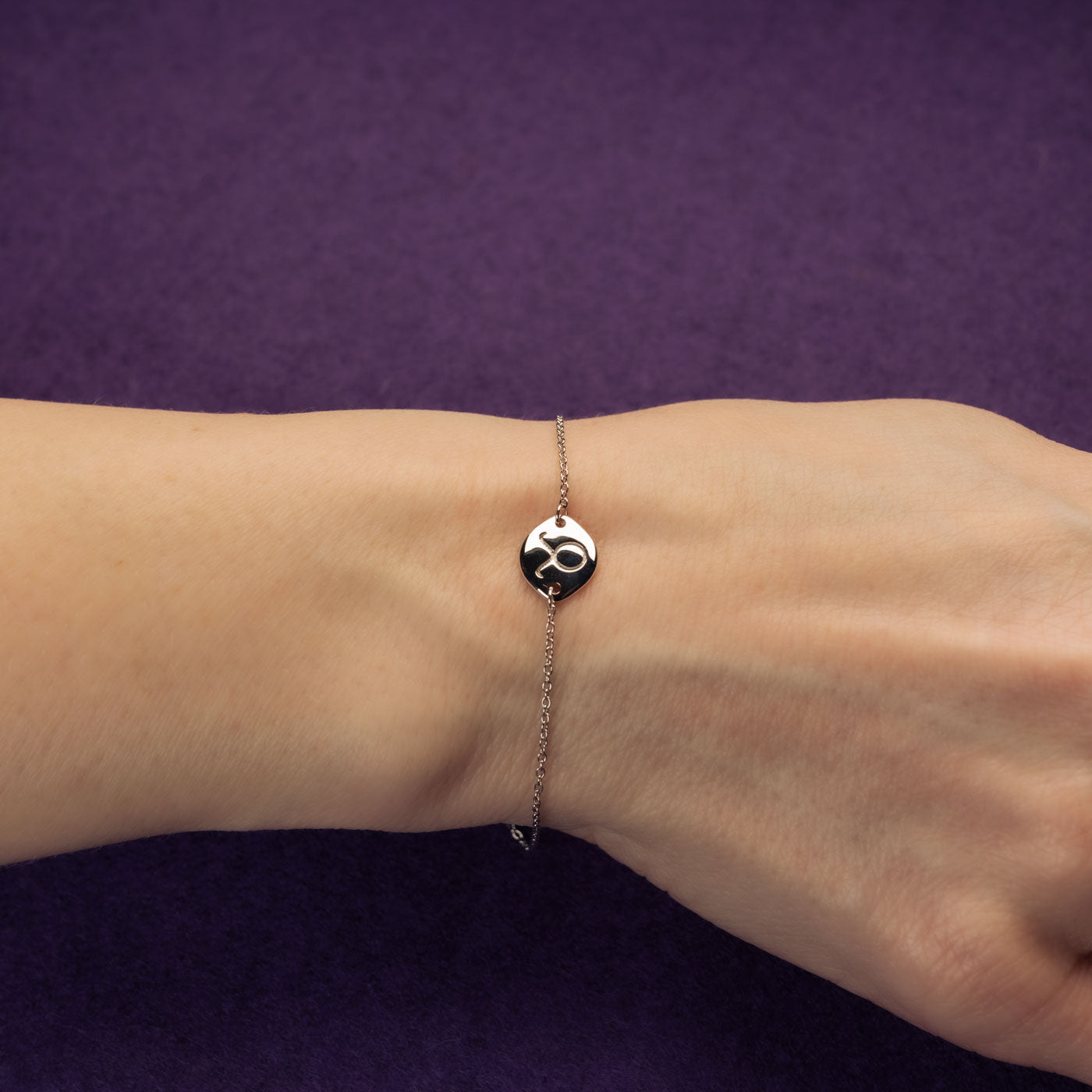 Delicate sterling silver bracelet featuring an adjustable chain with a polished Taurus zodiac symbol disc, styled on the wrist against a rich purple background.