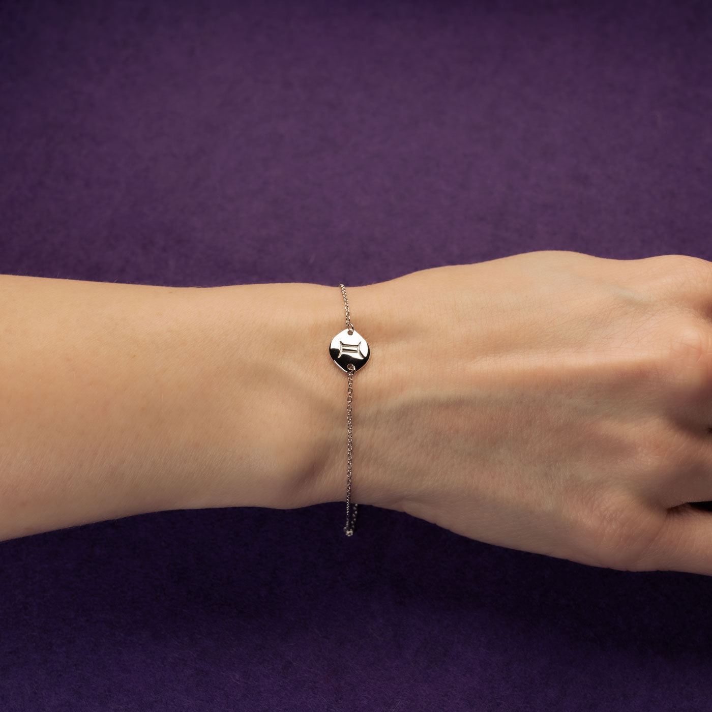 Delicate sterling silver bracelet featuring an adjustable sliding bead and a polished hexagonal charm engraved with the Gemini zodiac symbol, worn on the wrist.