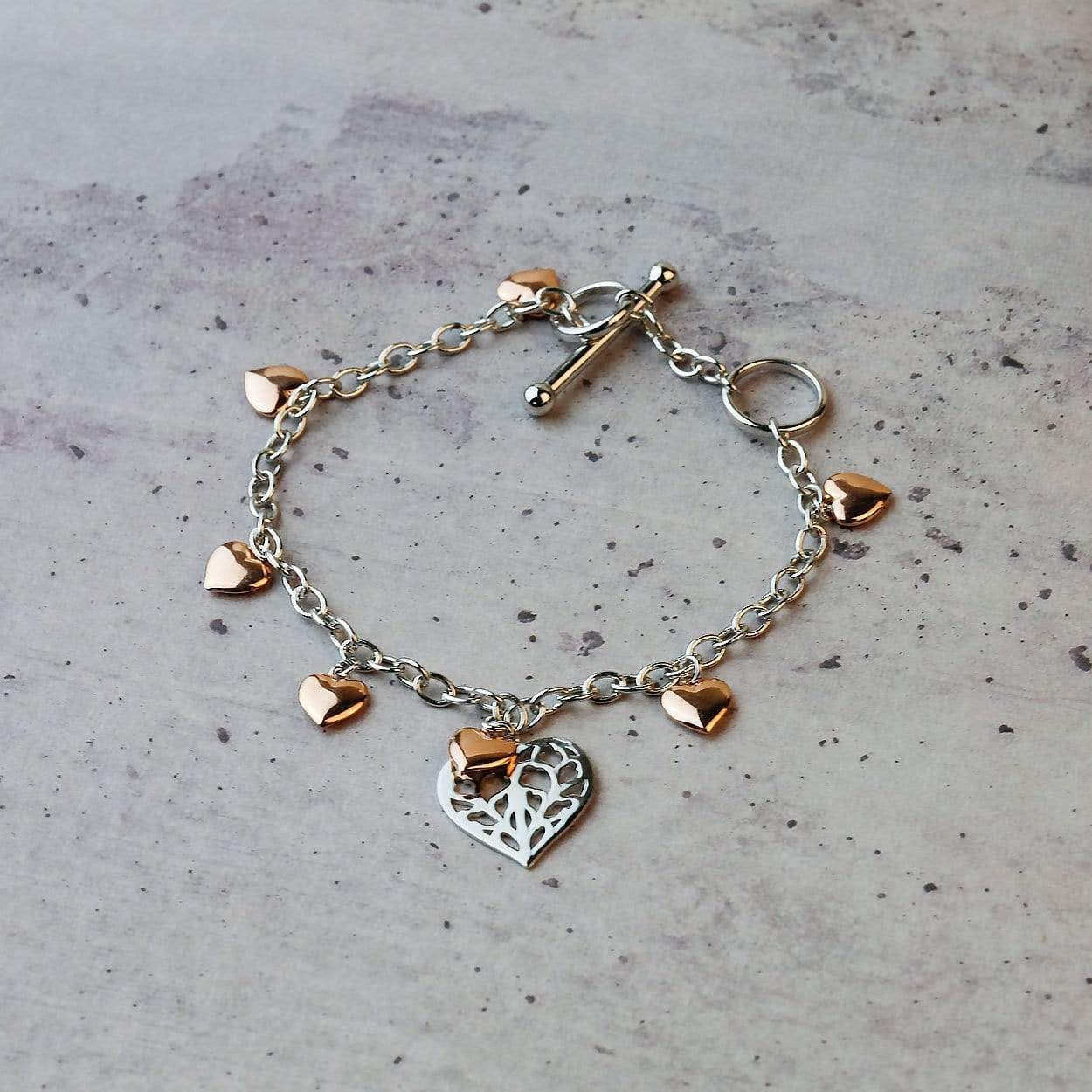 Delicate sterling silver bracelet featuring a T-bar fastening and adorned with rose gold vermeil heart charms, including a detailed openwork heart centerpiece.