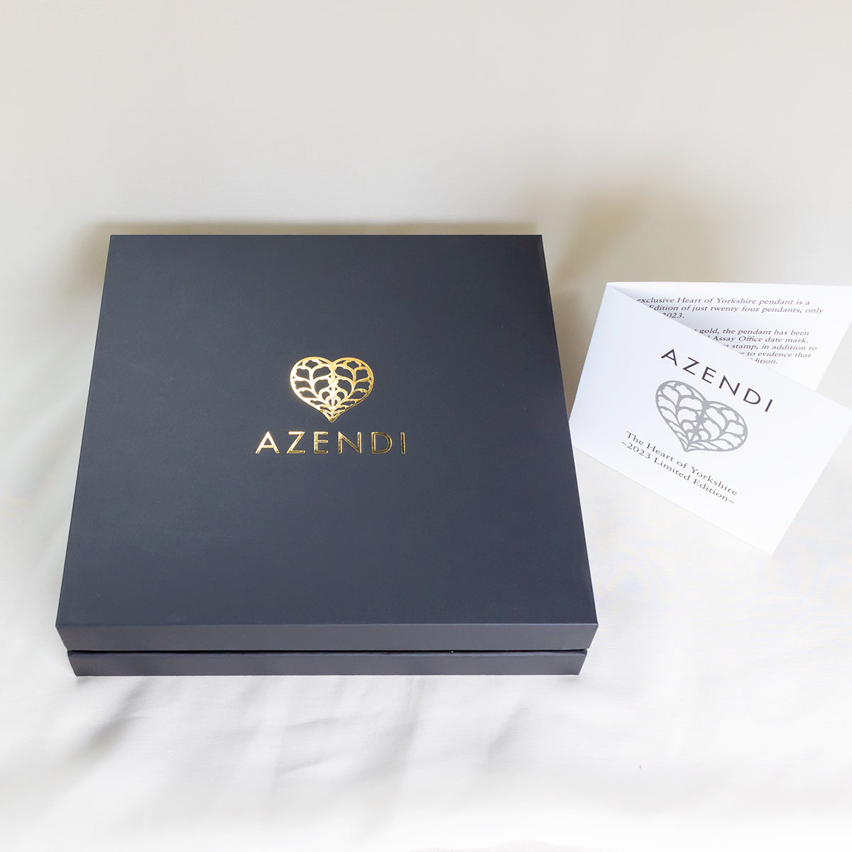 Elegant dark blue Azendi jewellery box with gold heart logo embossed on the lid, accompanied by branded informational cards featuring the Heart of Yorkshire motif.